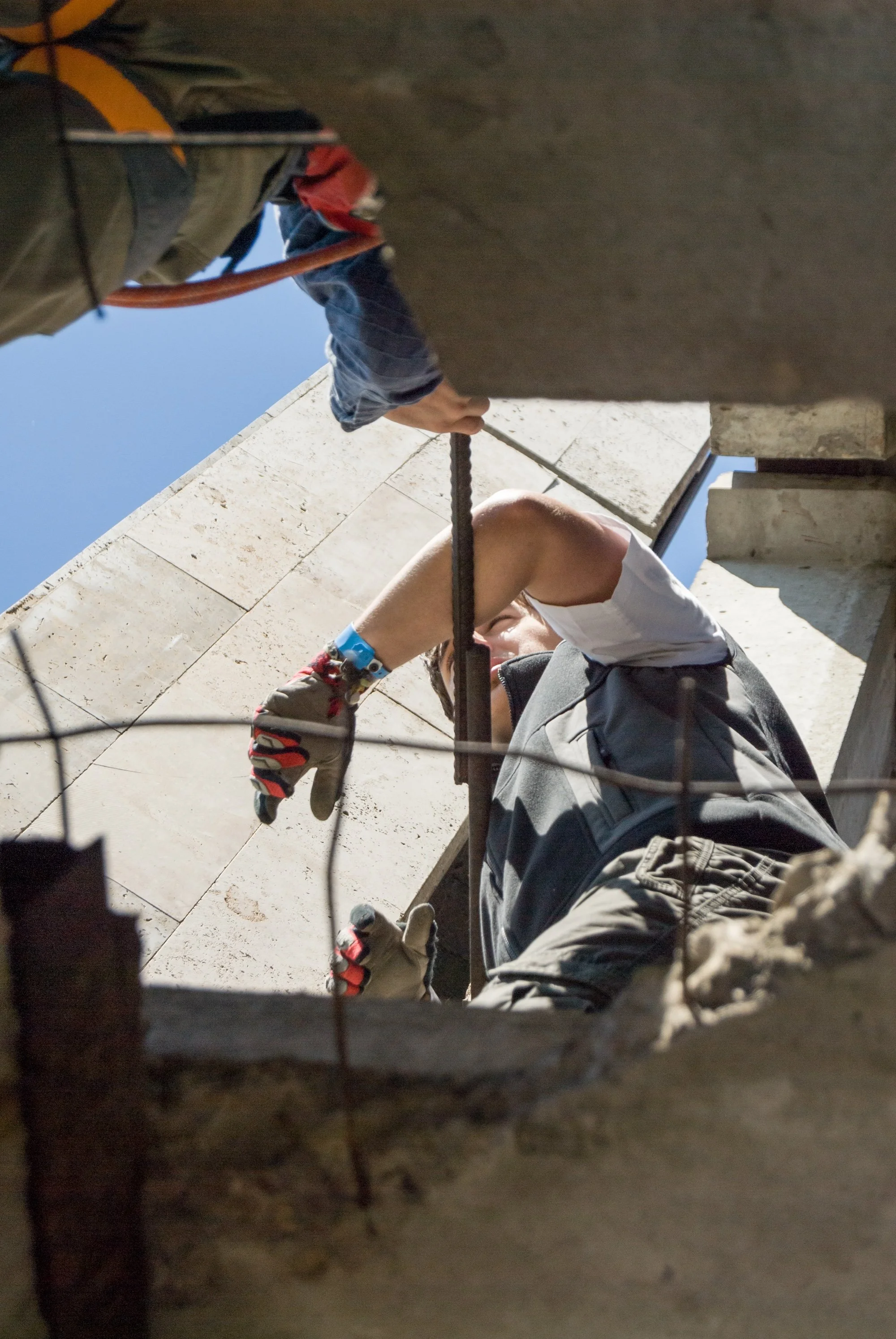 Person working on a construction site, viewed from inside a hole or opening in a wall, with tools and safety gear, and a concrete structure in the surroundings | Adelaide Insurance Builders | SA
