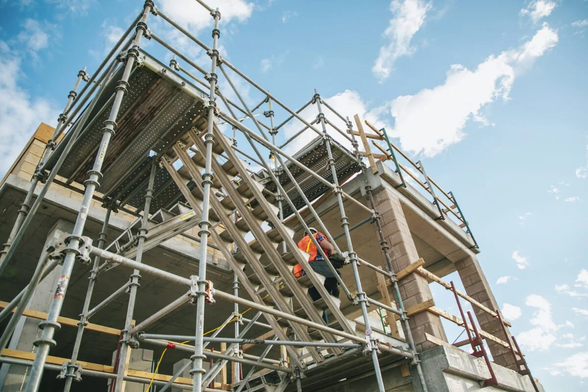 Construction worker in safety gear on scaffolding building a concrete structure.