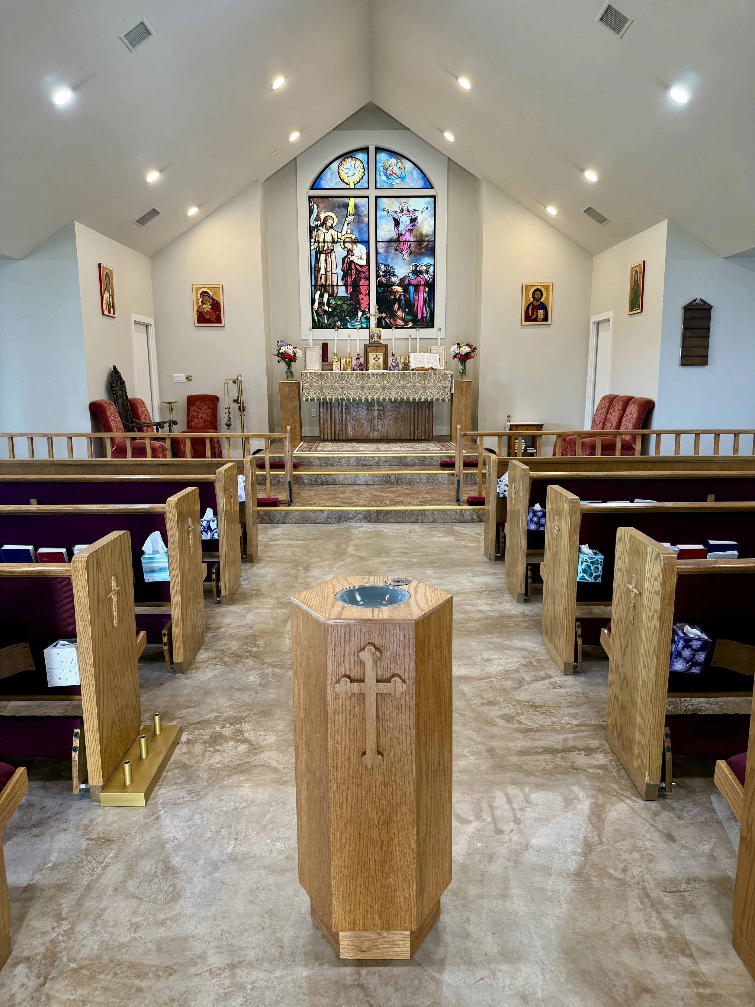 Inside St. Stepens church, wooden pulpit with a gold cross, pews facing an altar with a stained glass window depicting a biblical scene, and religious icons on the walls.