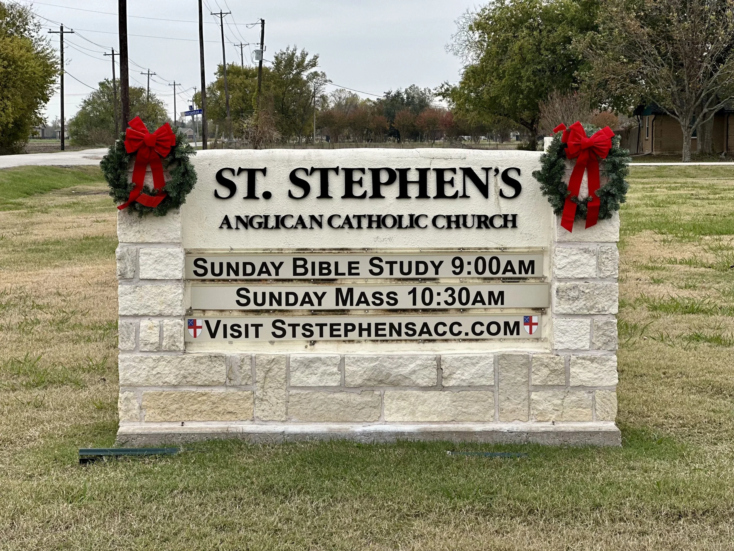 Sign for St. Stephen's Anglican Catholic Church decorated with Christmas wreaths with red bows, providing information about service times and website.