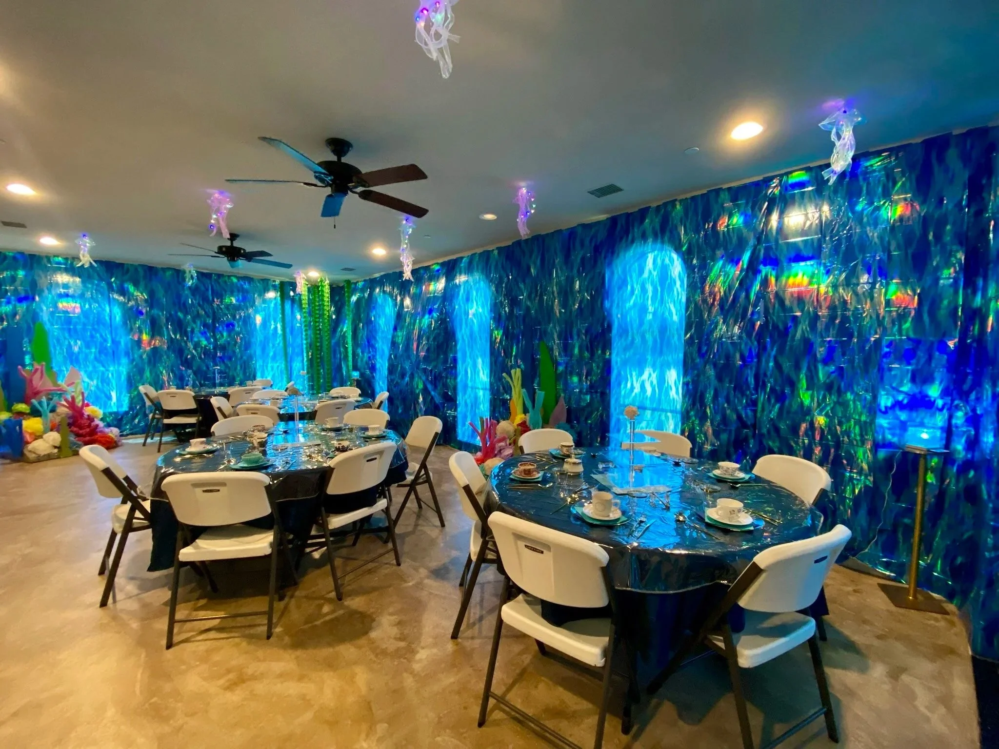 Ladies tea decorations in the parish hall with large iridescent wall decorations, tables set with dishes, and some decorations on the floor resembling coral.