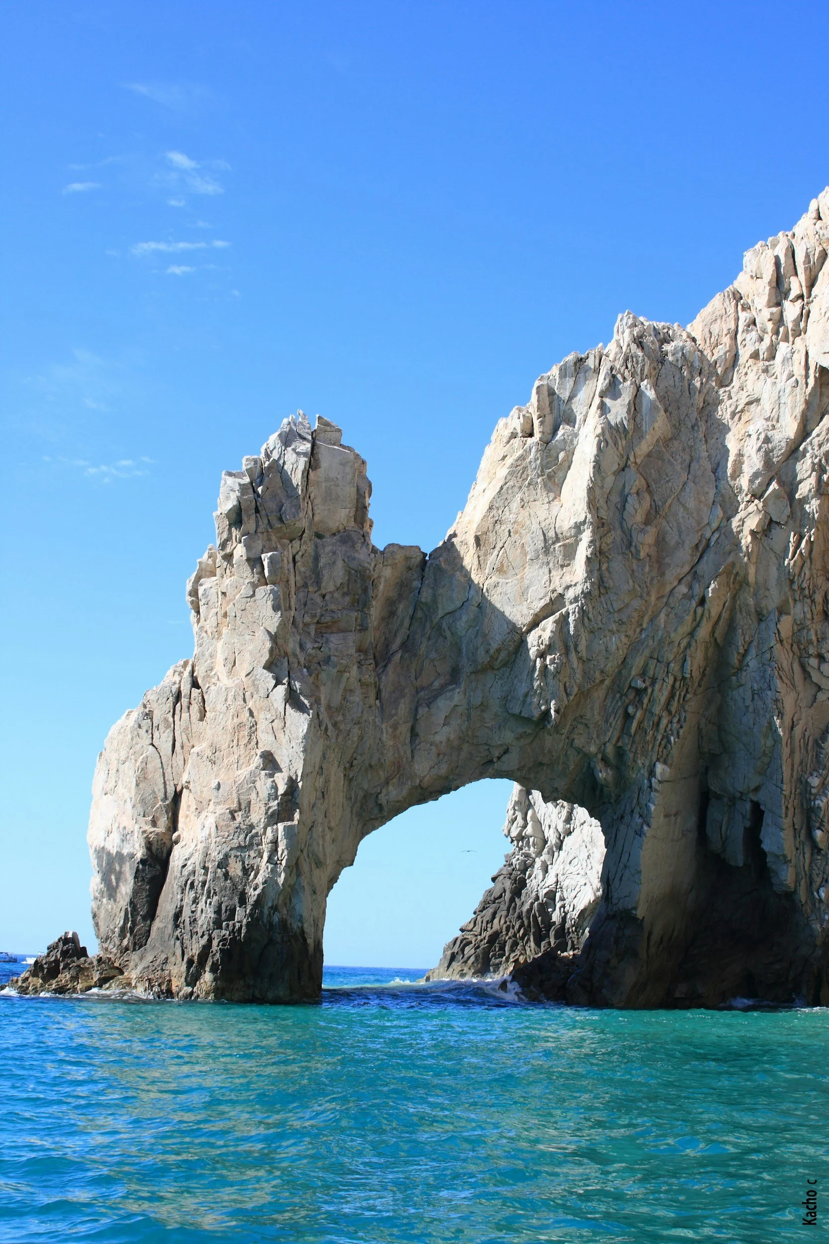Formación rocosa natural en forma de arco en el mar, con aguas azuladas y cielo despejado.