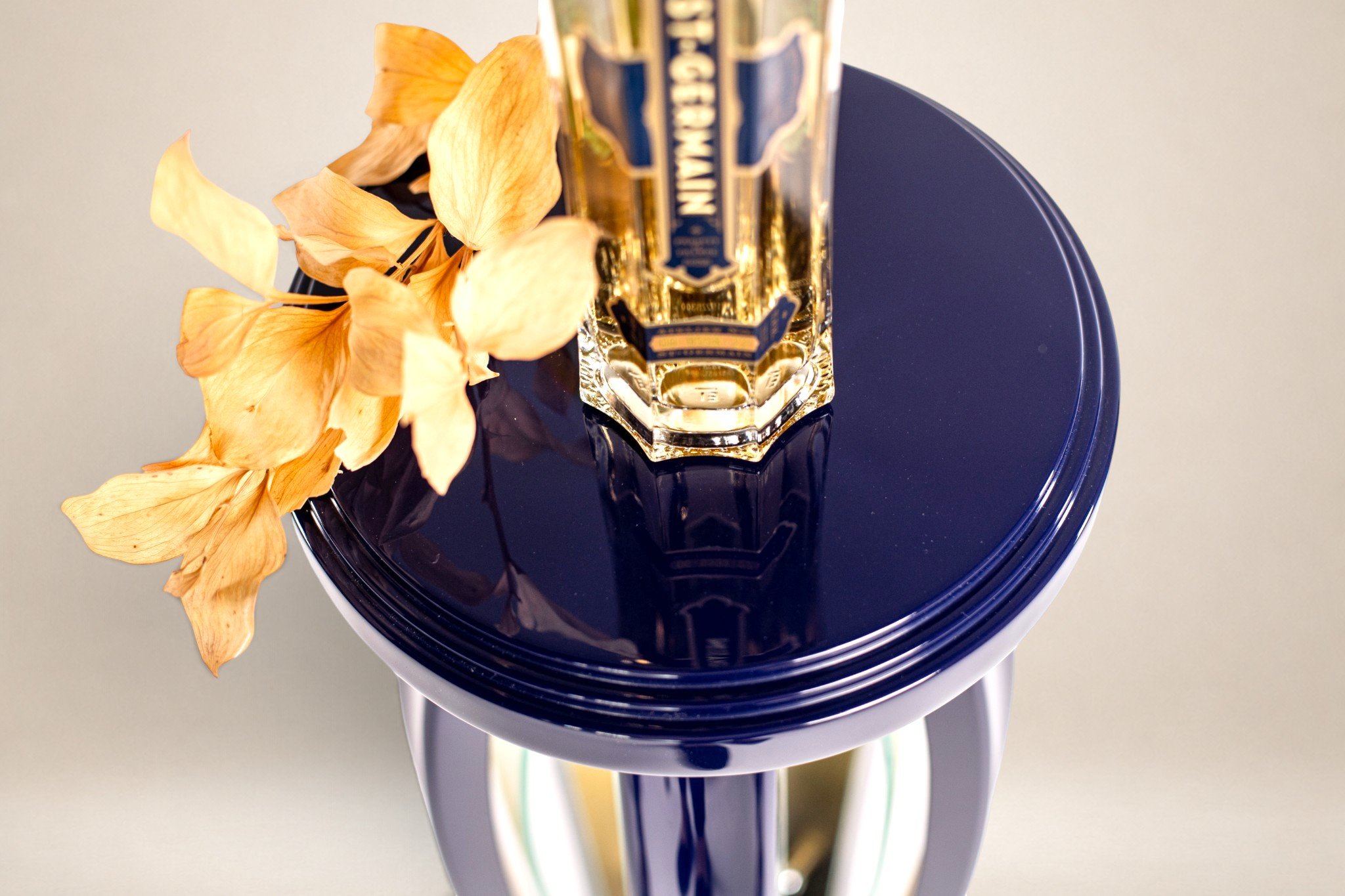 A bottle of St. Germain on a blue table with dried hydrangea flowers next to it