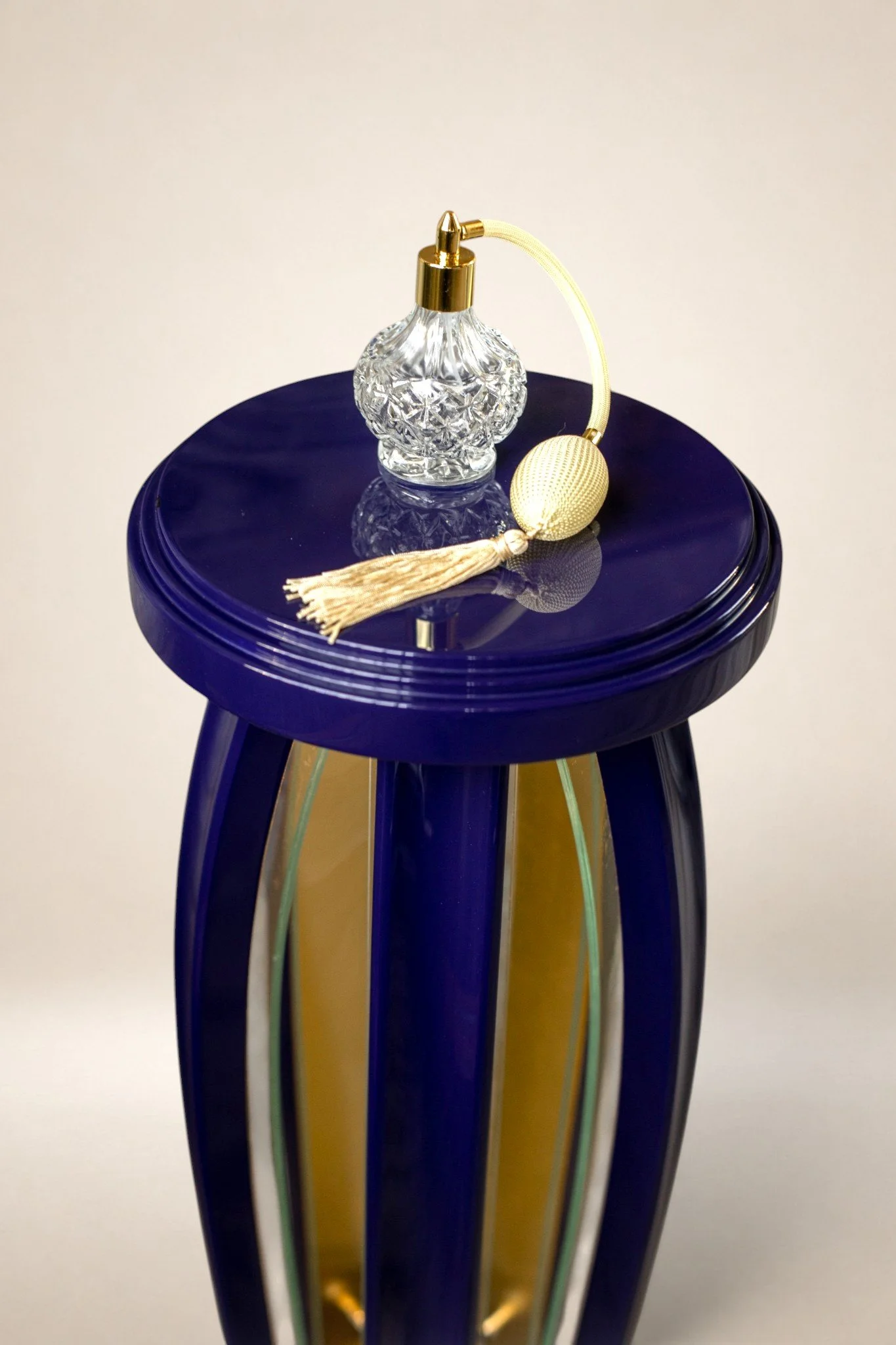 A decorative glass perfume bottle with a gold cap and a yellow tassel, placed on a blue and 24k gold table.