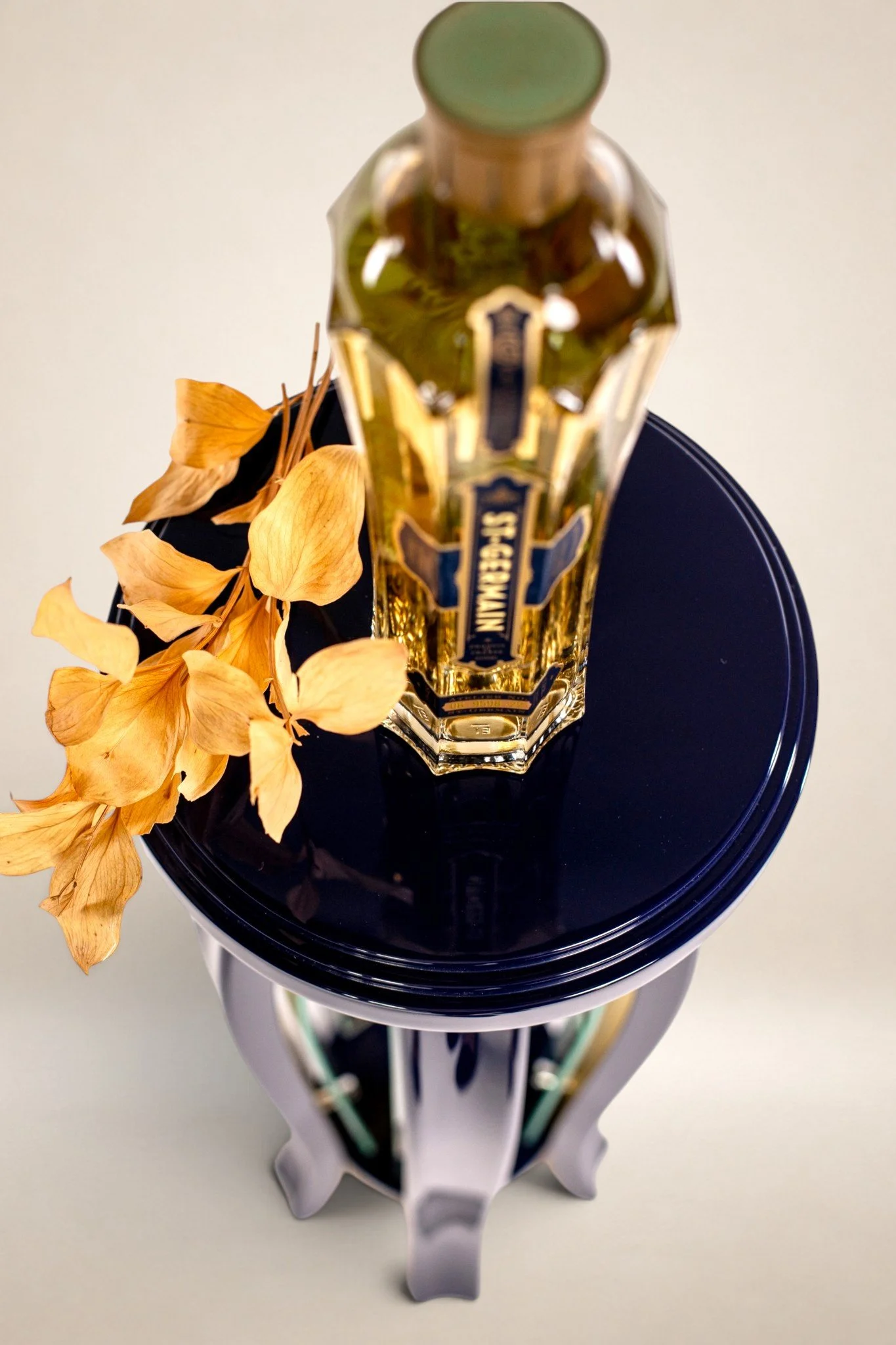 A decorative table with a glass bottle of St. Germain and dried yellow flowers on top.