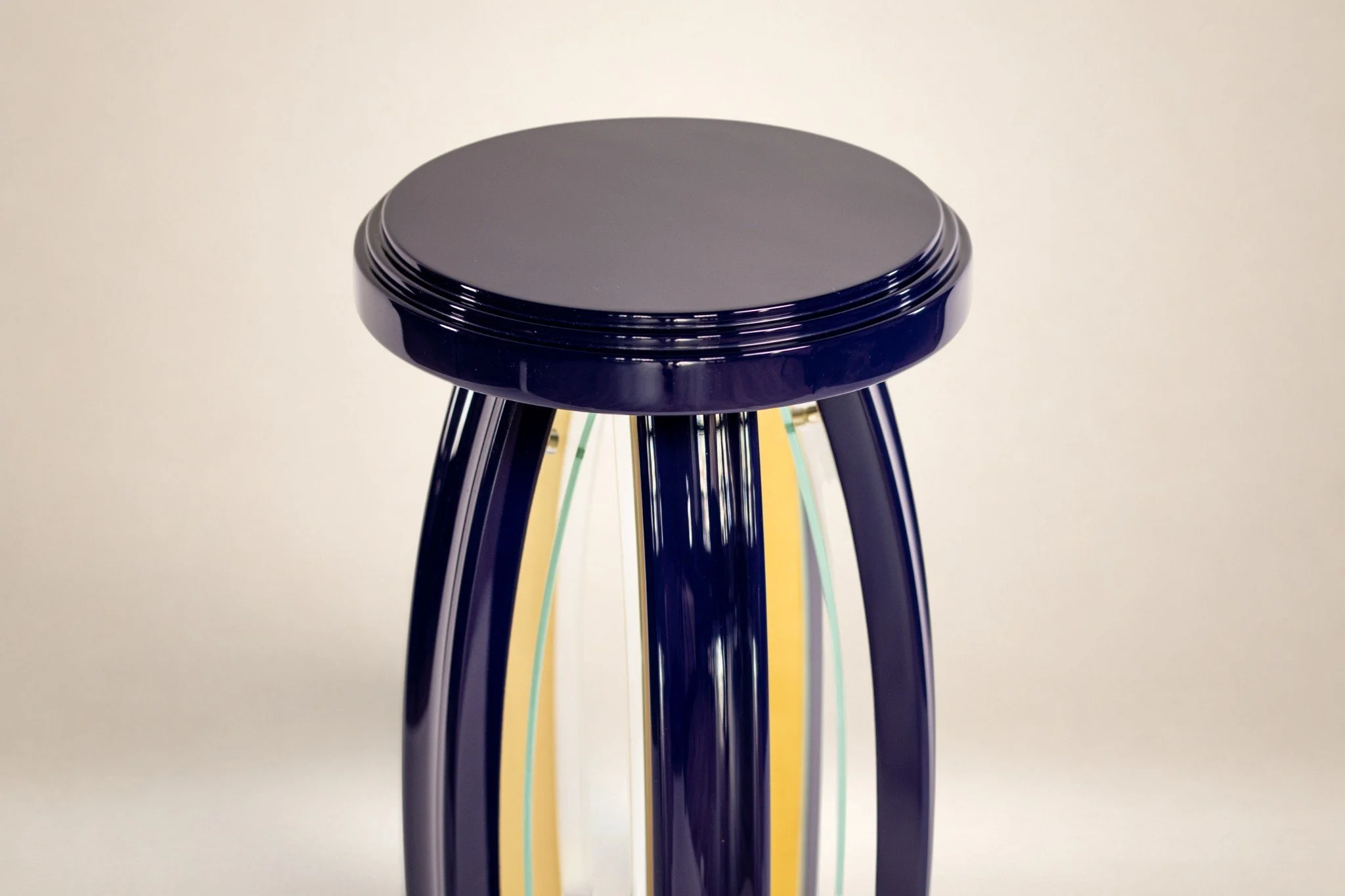 A black stool with a round cushioned seat and multiple colorful legs in shades of yellow, green, blue, and black, against a plain white background.