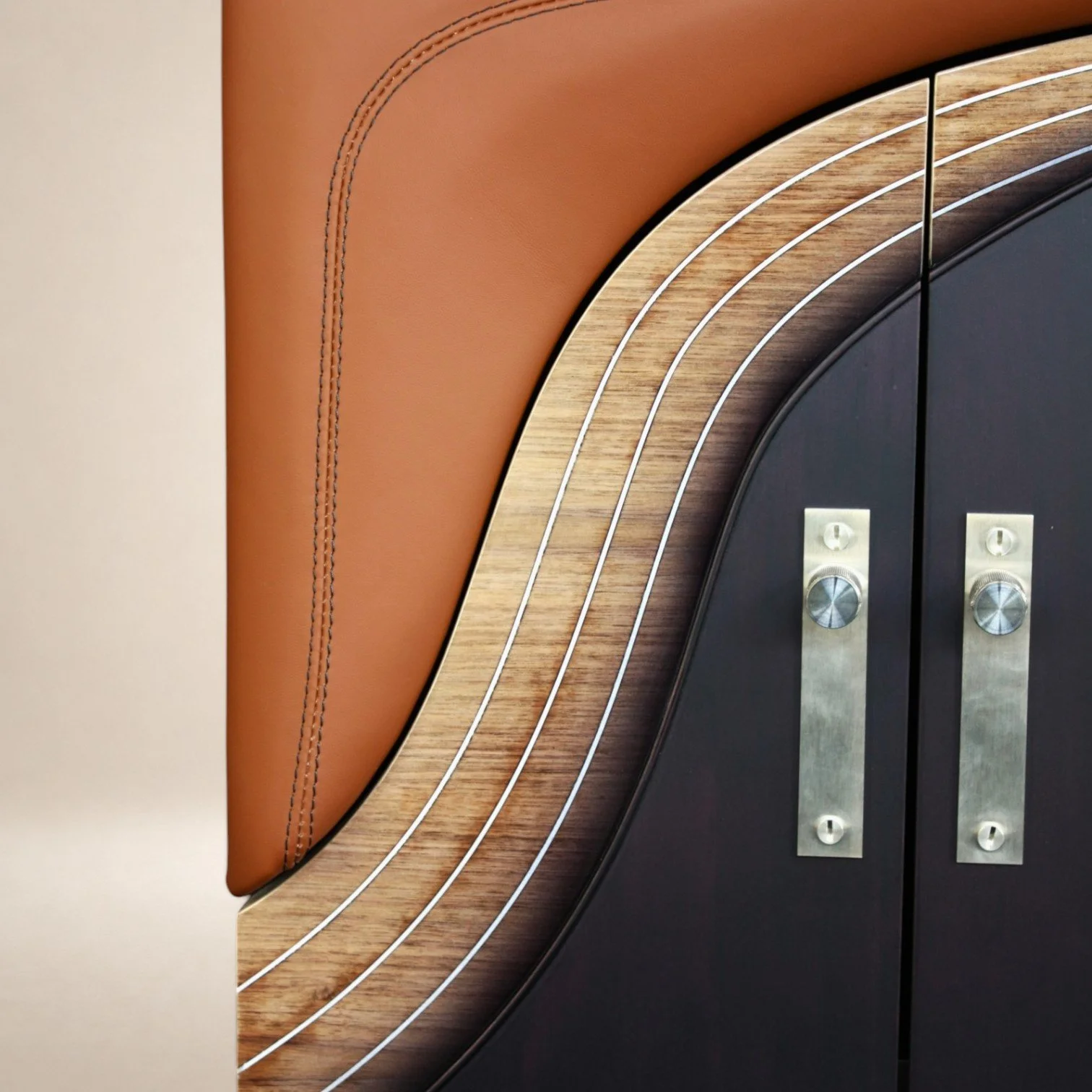 Close-up of a portion of a modern furniture piece with a curved design, featuring a leather cushioned section, wooden accents with white lines, and metal hardware.
