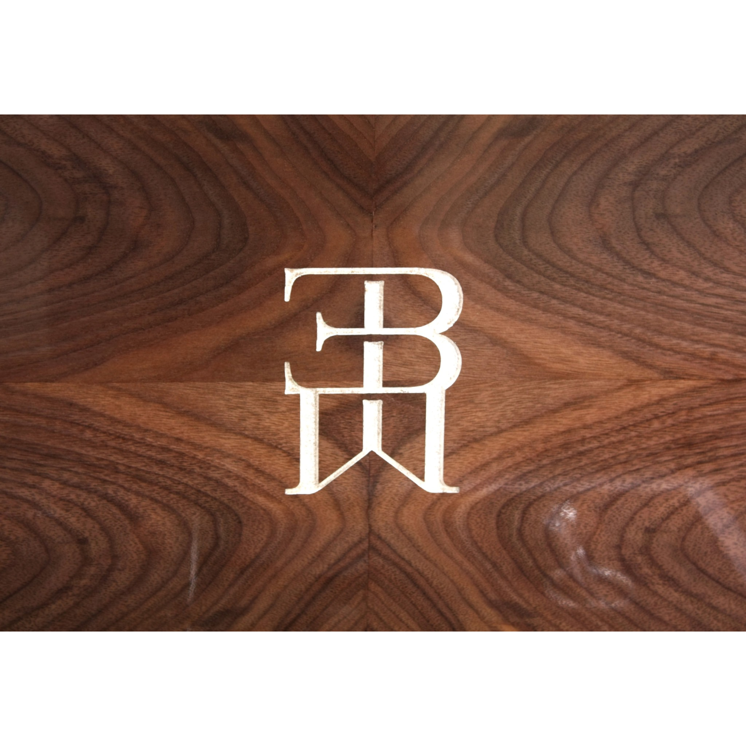 Close-up of a wooden surface with a white metal emblem featuring the letters B and E intertwined.