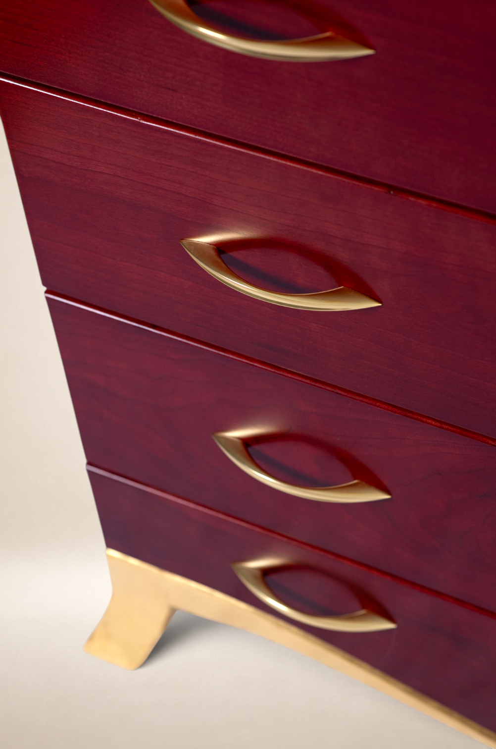 Close-up of a red wooden chest of drawers with gold-colored handles and legs.