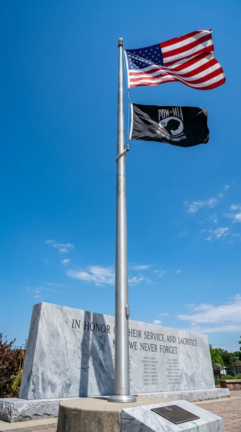 American flag and POW/MIA flag flying above a marble memorial with an inscription in honor of service members.
