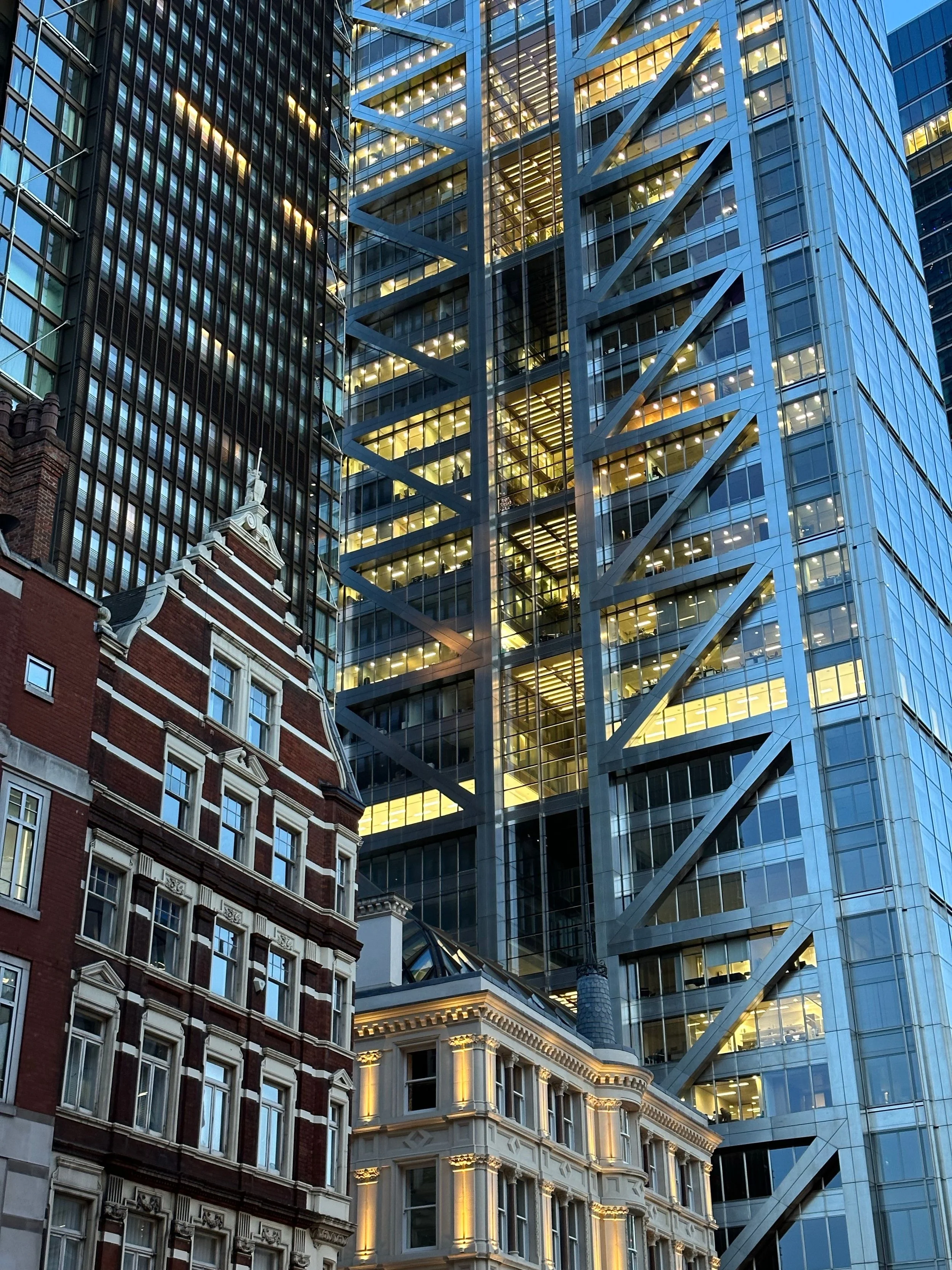 Combination of historic and modern skyscrapers in an urban cityscape, with illuminated windows and architectural details.