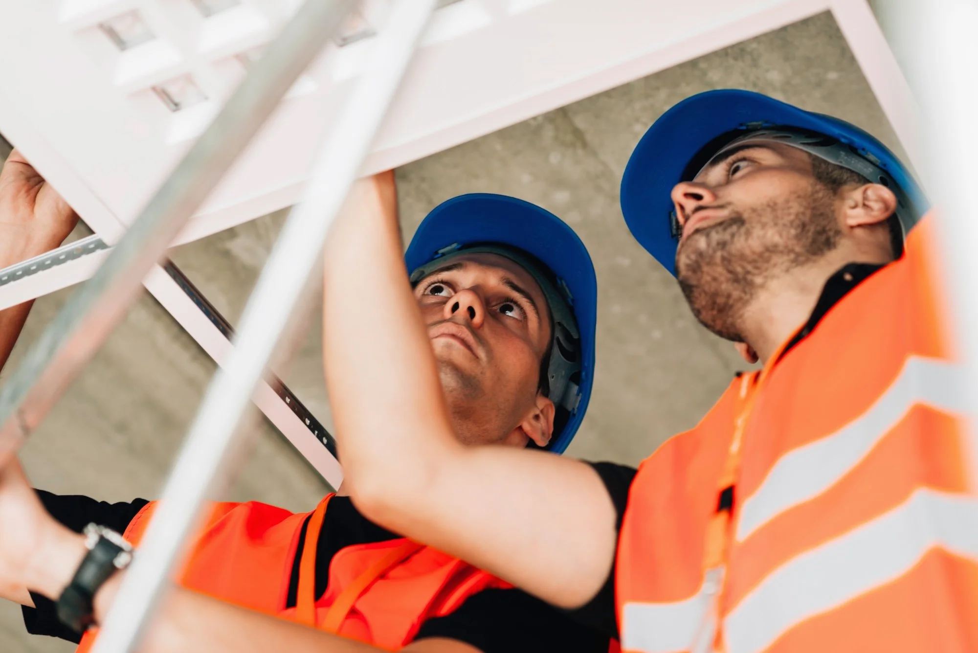 Construction workers wearing blue helmets and orange safety vests working at a site.