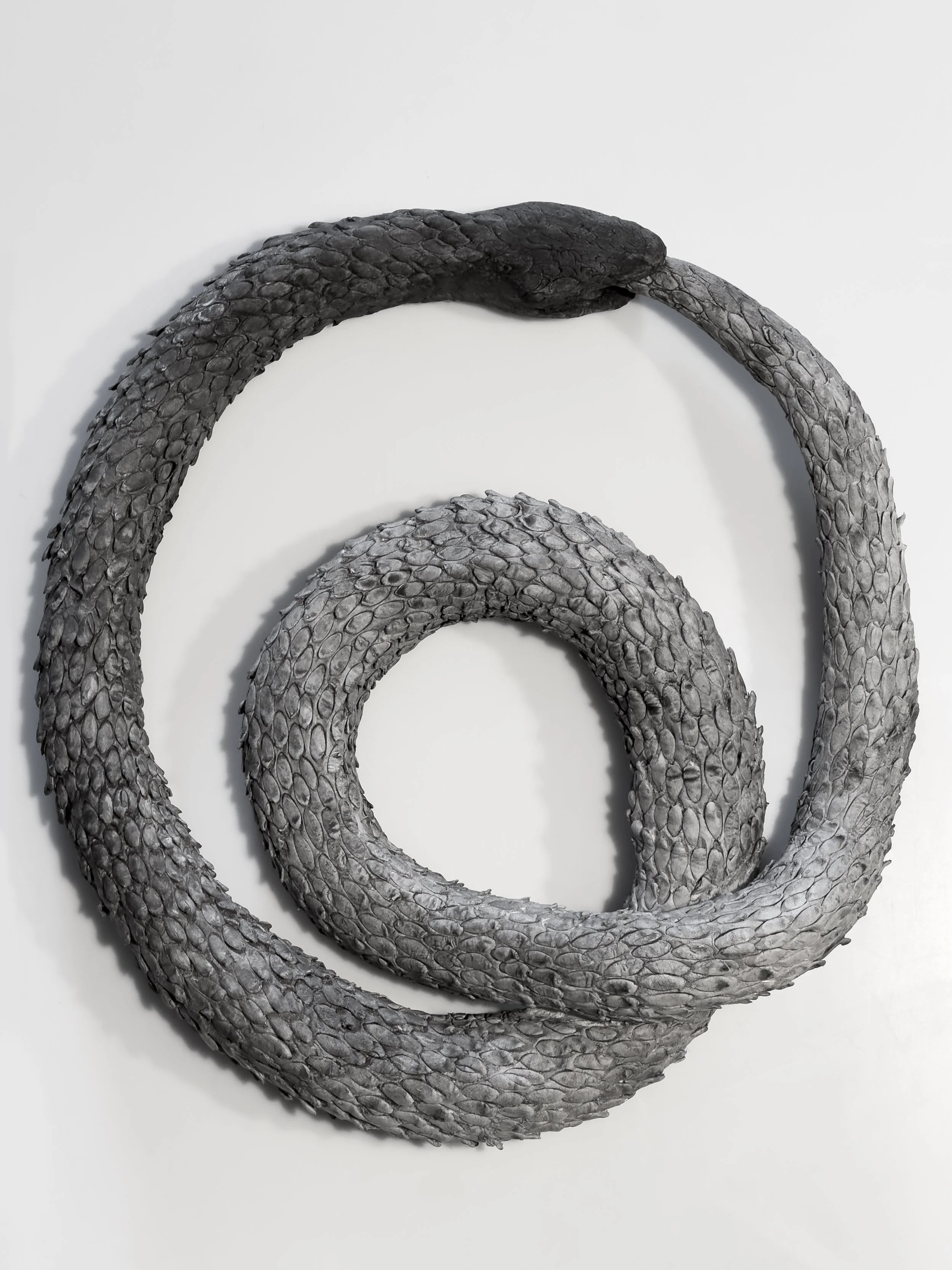 Ceramic Ouroboros sculpture from Archive of Extraction, a tail-eating serpent symbolizing cyclical repetition in memory and technology.