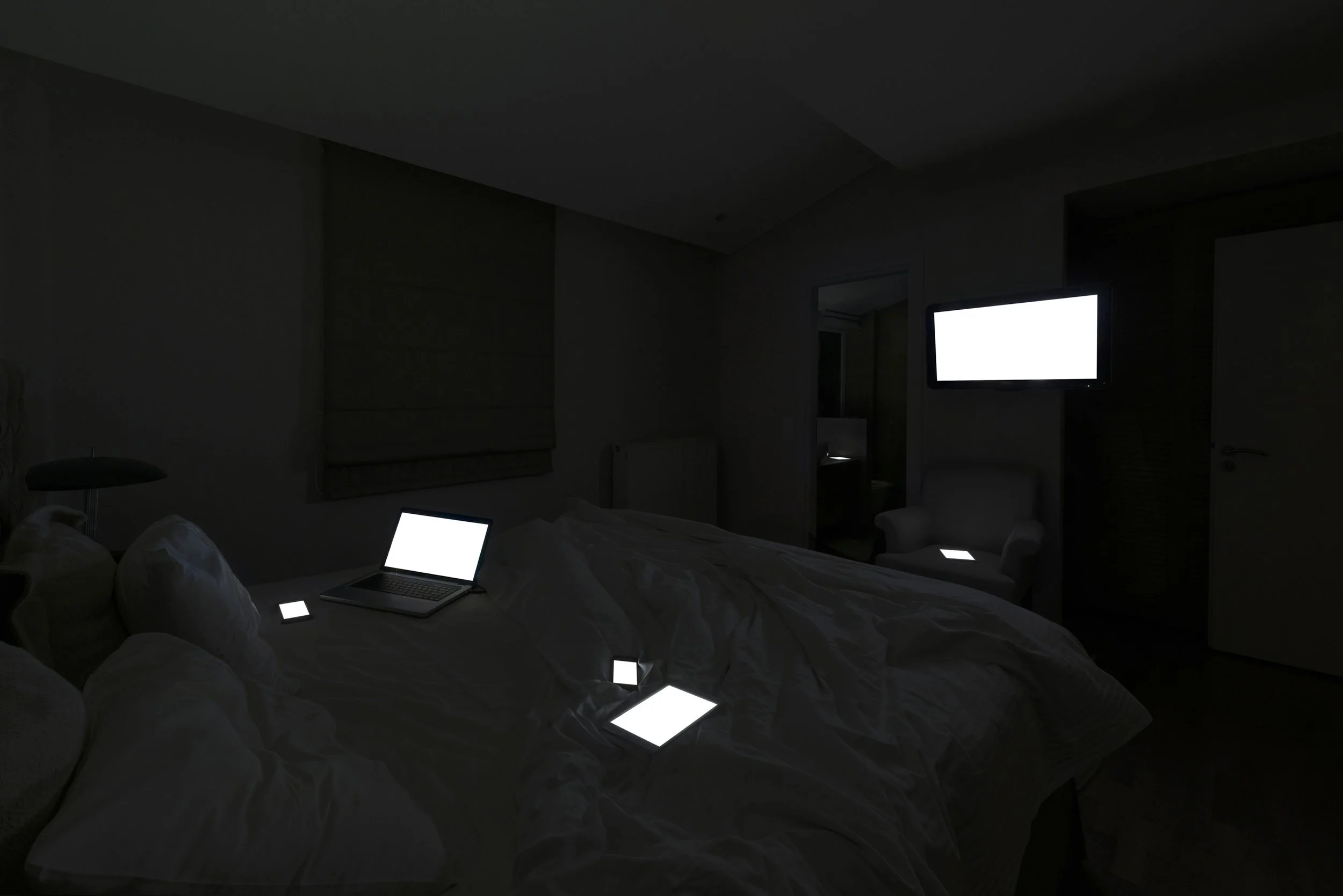 Breakfast in Bed from Family Portraits by Maria Mavropoulou, showing illuminated devices in an intimate bedroom setting and questioning whether screens replace lovers, friends and family.