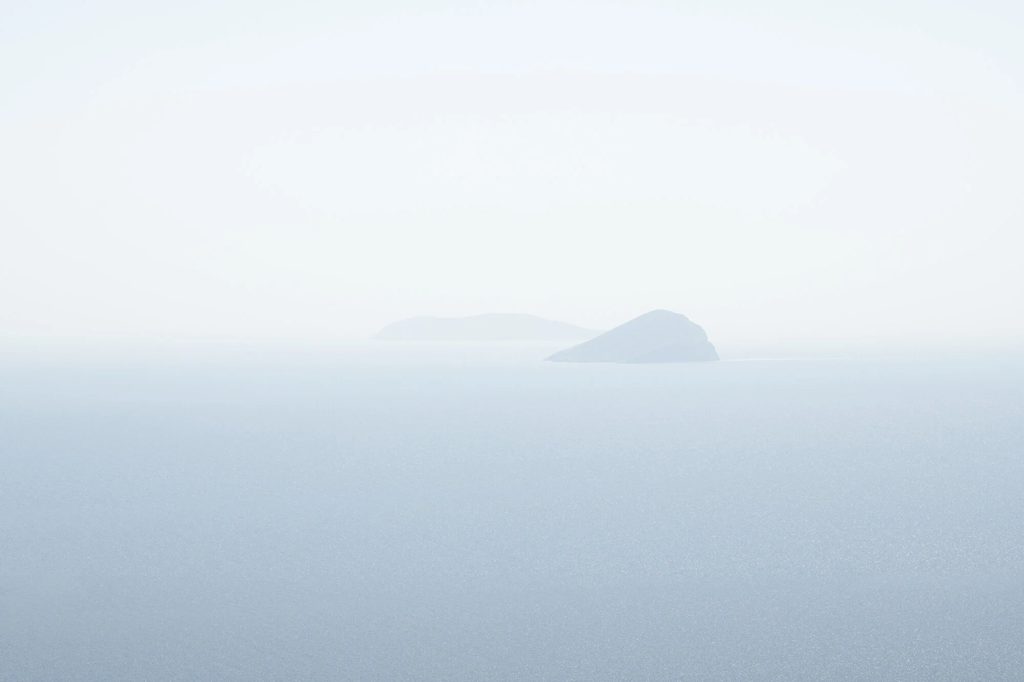 Archive photograph used to train the algorithm for A Thousand Ithacas, showing two hazy island silhouettes almost disappearing into a pale blue sea and sky.