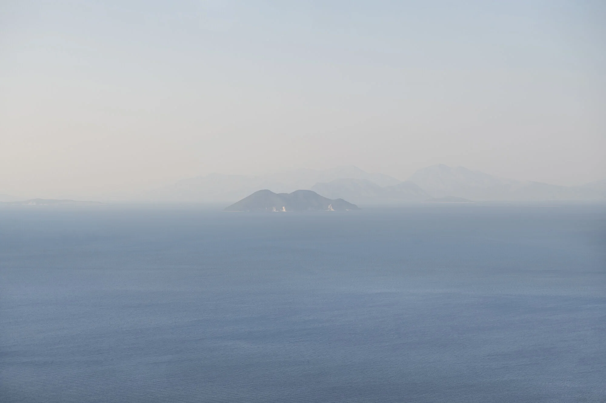 Archive training photograph for A Thousand Ithacas, showing several distant islands fading into blue atmospheric haze across the sea.