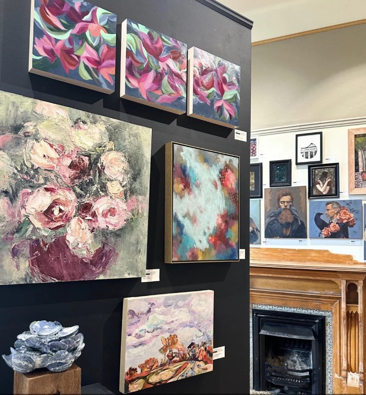 Colorful contemporary paintings displayed in an art gallery beside a decorative fireplace and sculpture