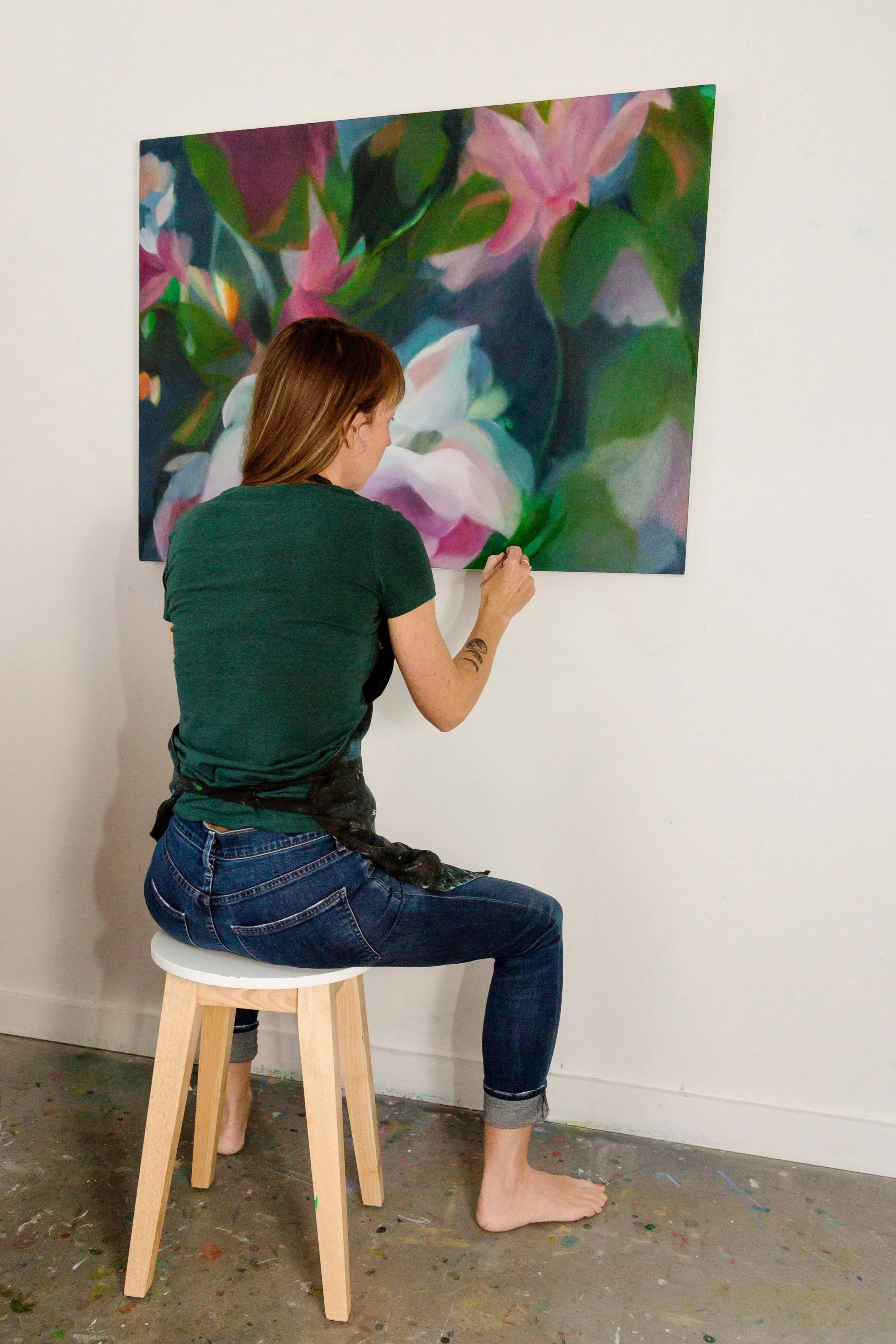 Artist sitting on a stool and painting a colorful floral artwork on a large canvas