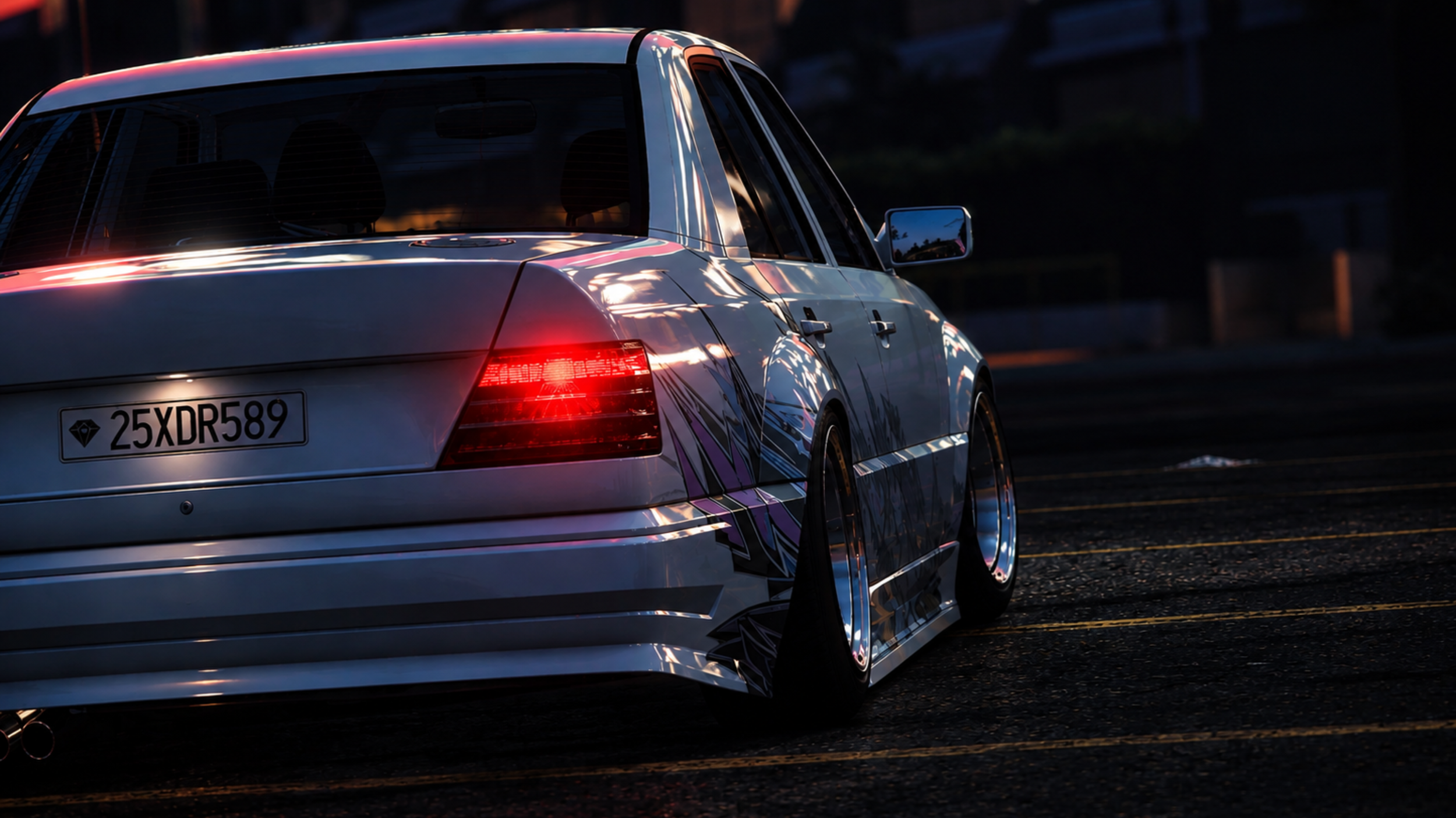 A white car with colorful decals on the side, parked on a dark asphalt surface at dusk, with its rear lights illuminated.