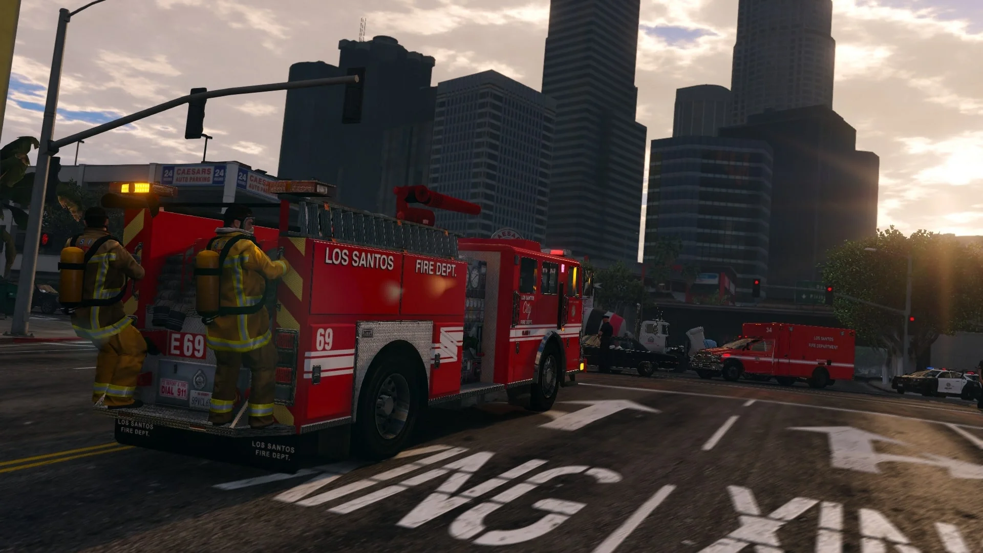 Firefighters in yellow gear working with a red fire truck from Los Santos Fire Department on a city street at sunset, with tall buildings in the background.
