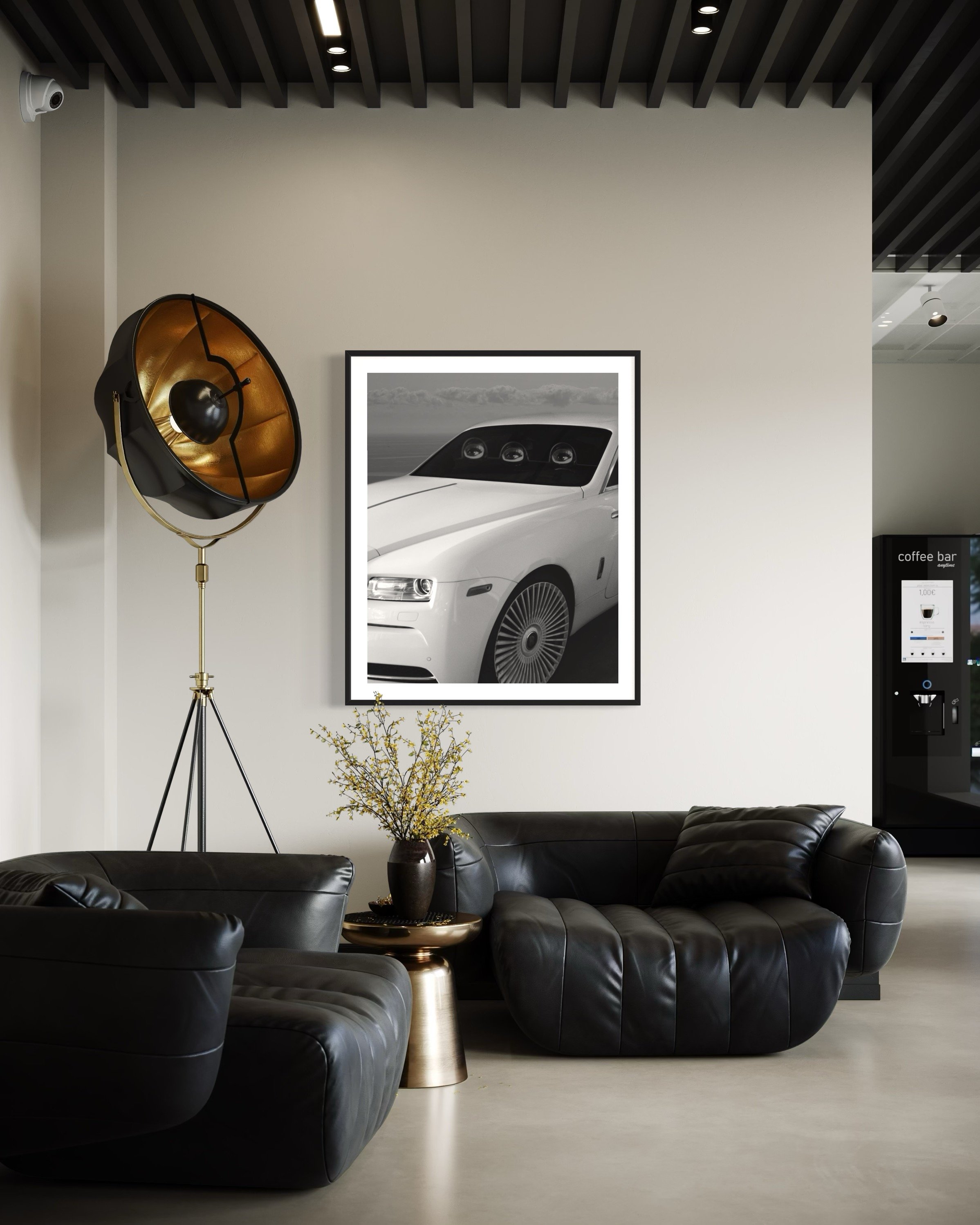 Modern lobby area with black leather sofas, a gold side table, a potted plant with yellowish leaves, a framed black and white car photograph, a vintage style floor lamp with gold and black finish, and a vending machine in the background.