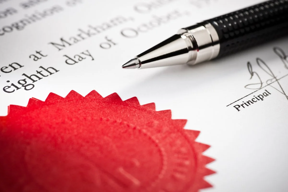 A close-up of a signed official document with a black pen and a red seal.