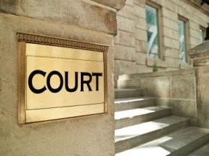 Gold-colored sign with black text that reads 'COURT' mounted on a stone wall outside a courthouse.