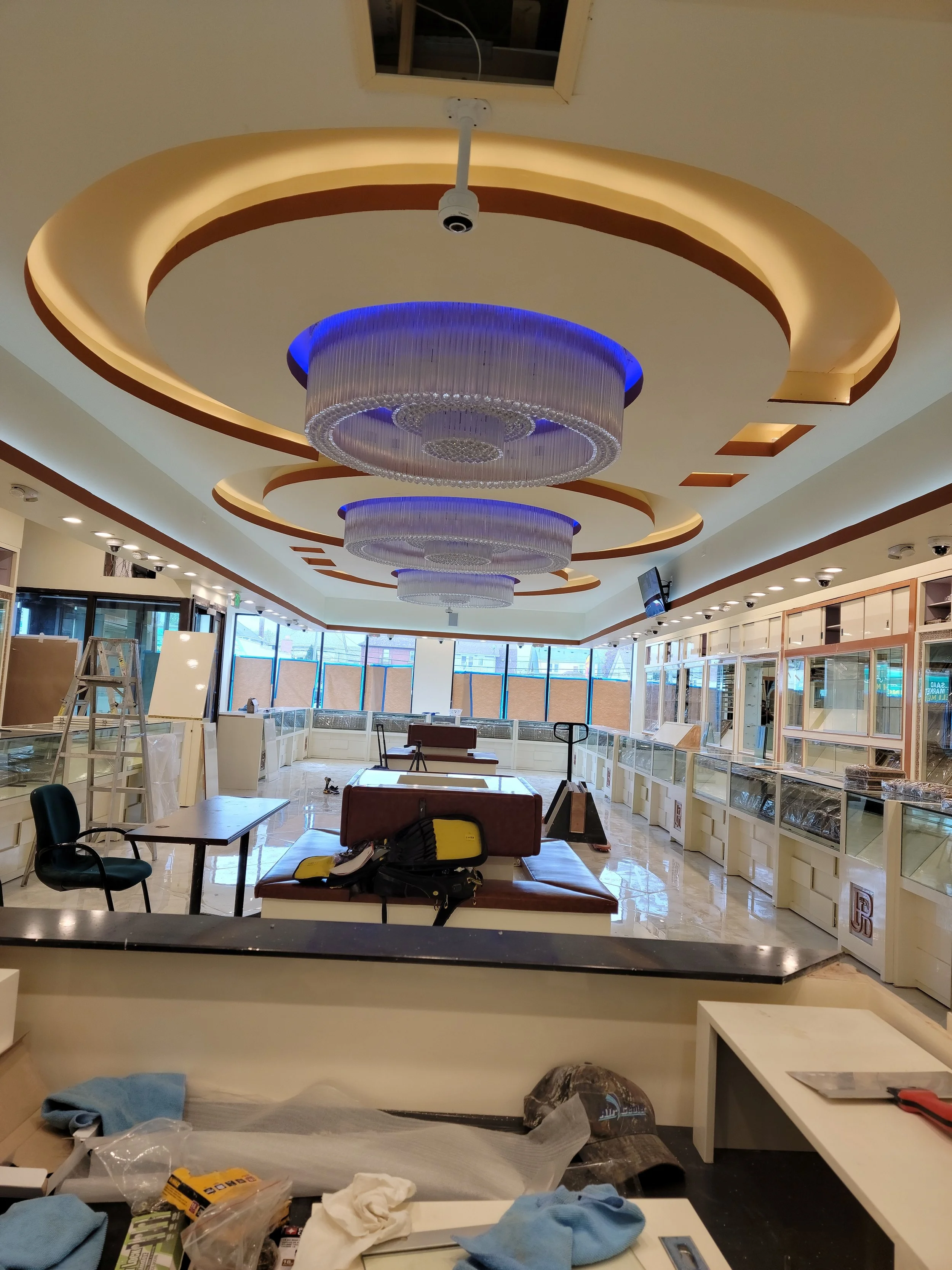 Interior of a store or showroom with ceiling lights and displays, with items and tools scattered in the foreground, indicating ongoing setup or renovation.