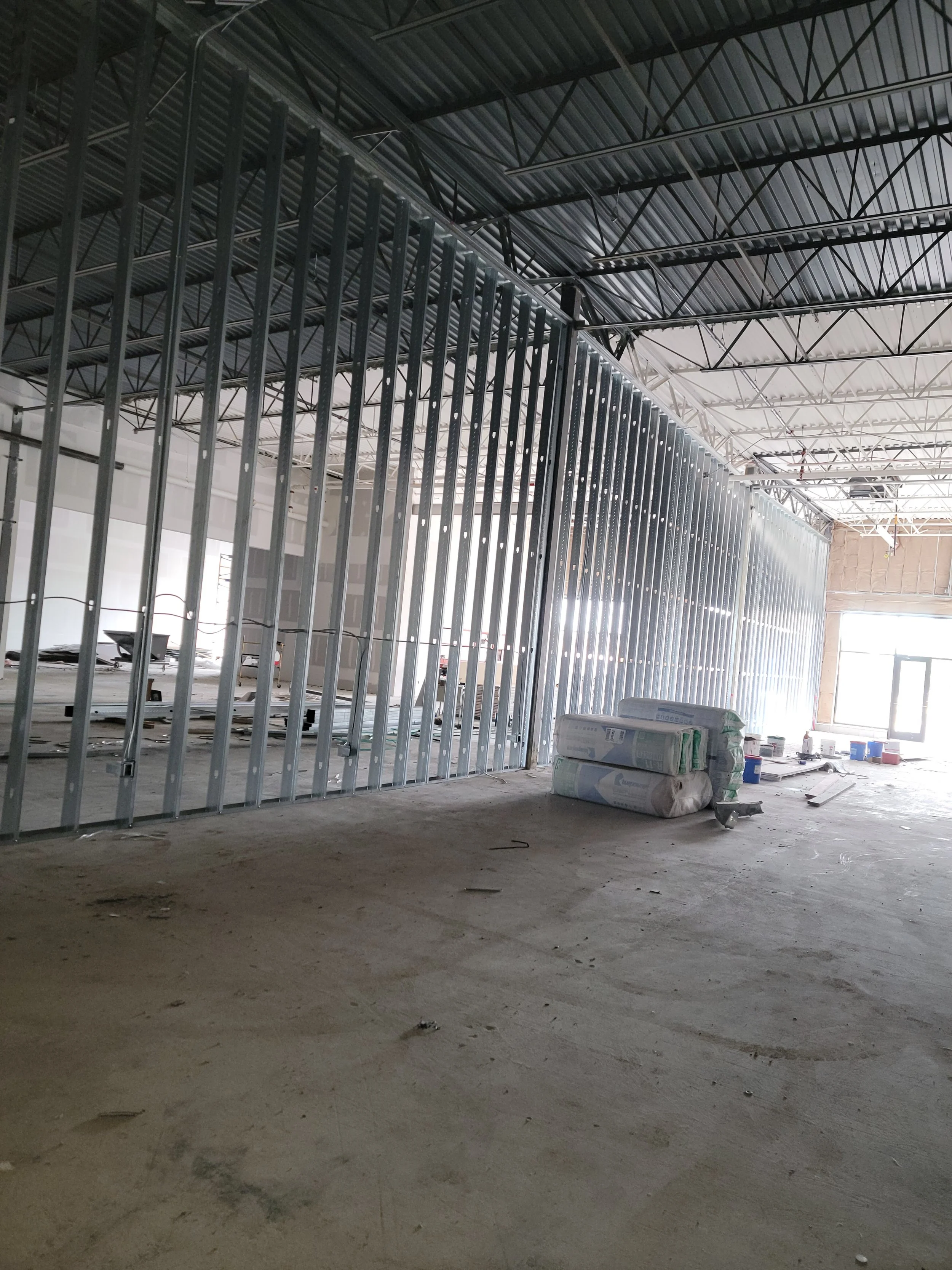 Construction site with metal framing for walls, construction materials, and equipment in a large open space with high ceilings.