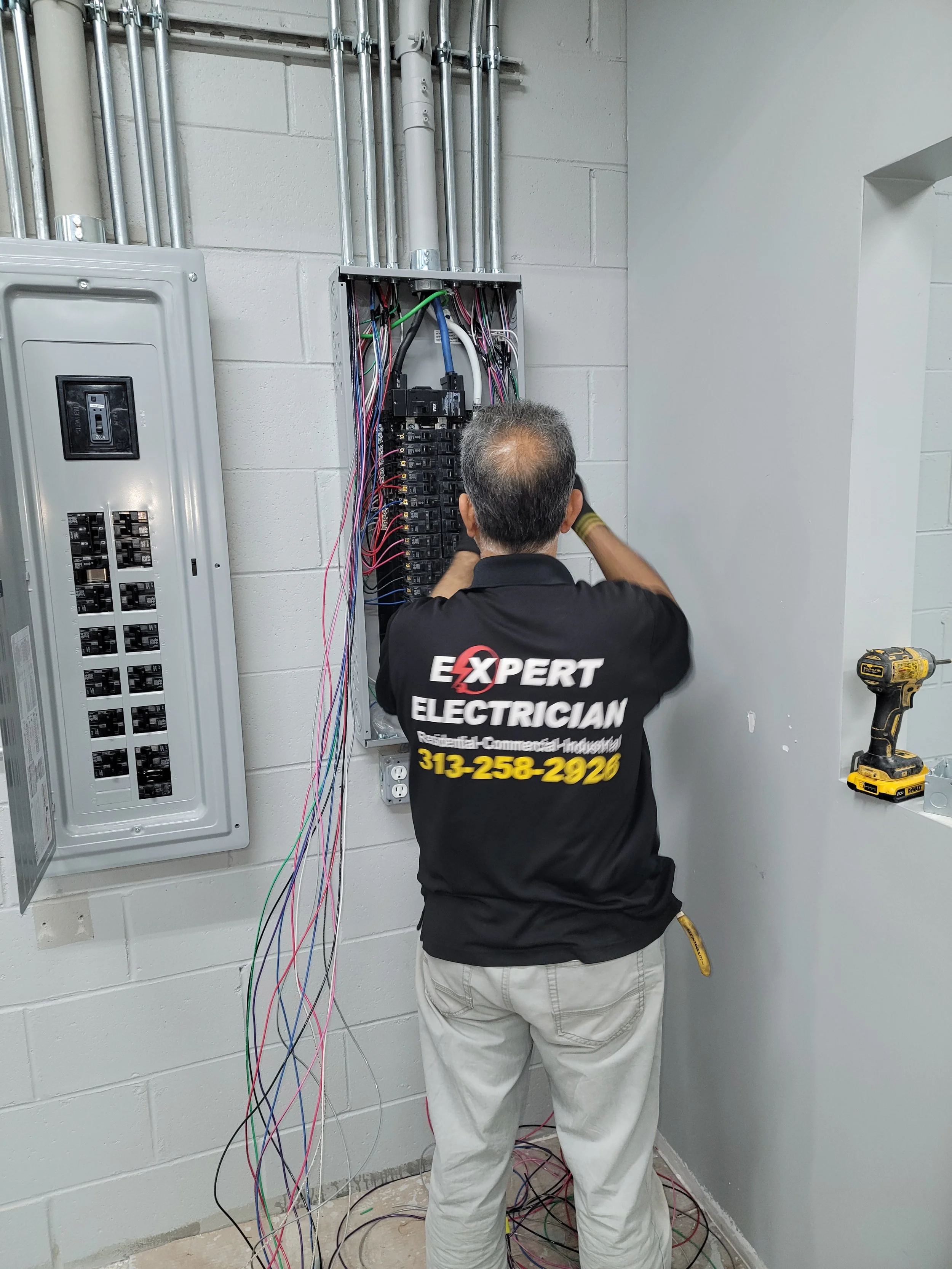 An electrician working on electrical wires inside an open electrical panel, with tools and wiring visible, in an indoor setting.