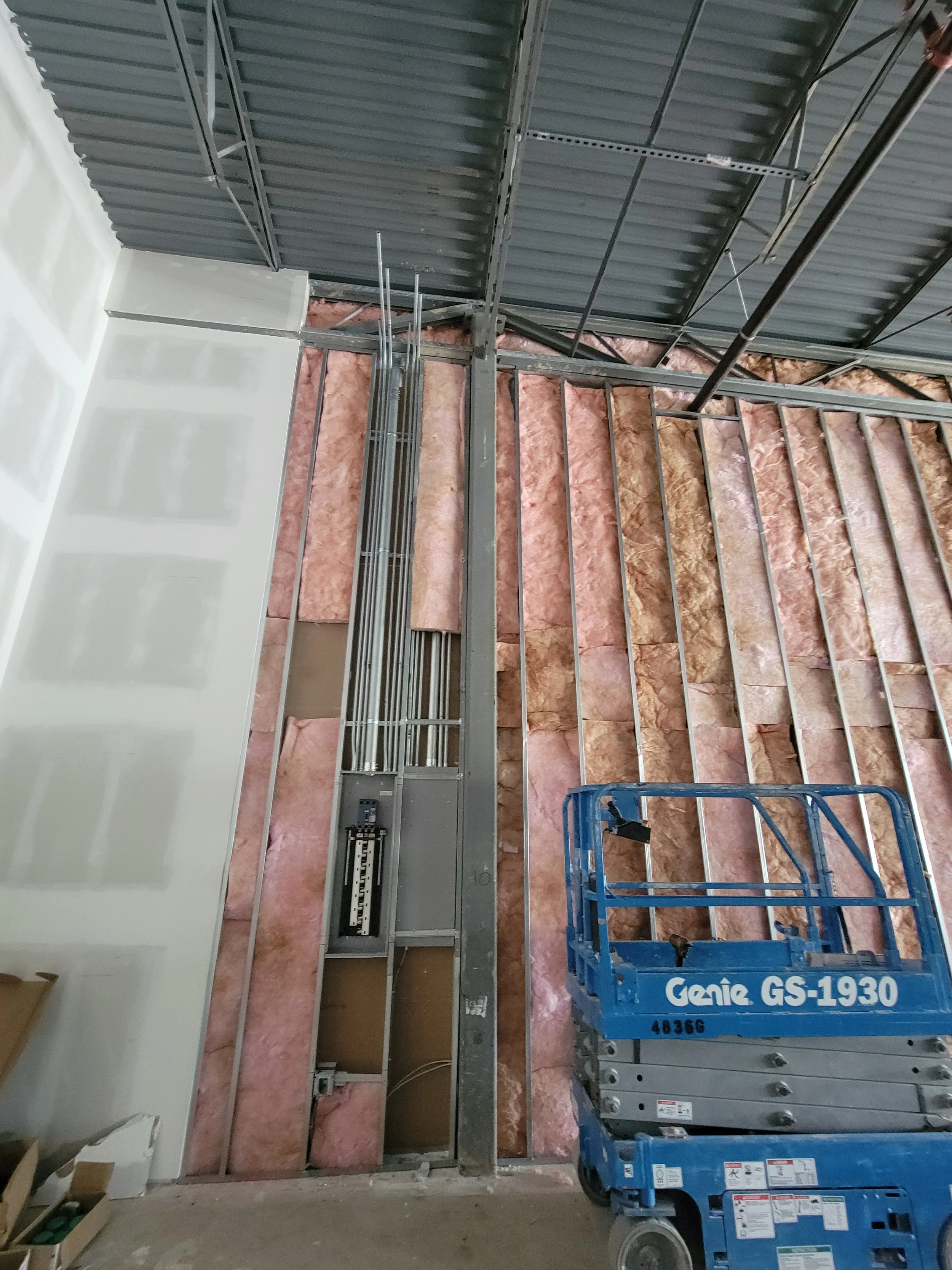 Construction site with metal framing, pink insulation, and a blue Genie lift.