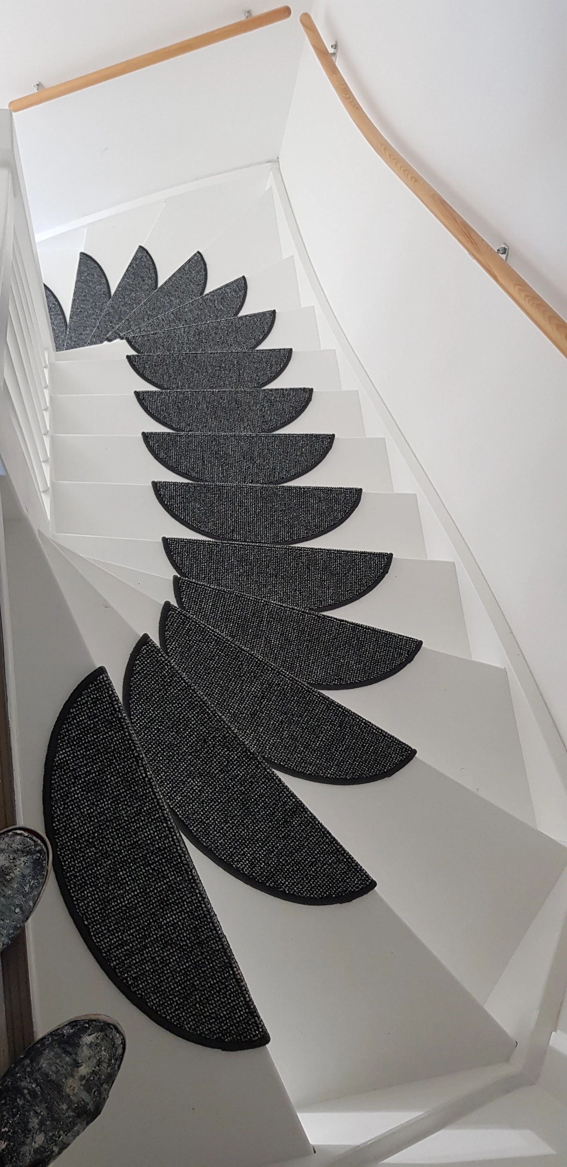 Black and white stair runner with a textured pattern on a white staircase with a wooden handrail.