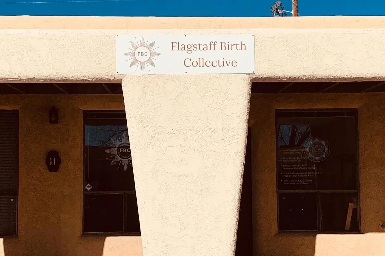 Sign that reads 'Flagstaff Birth Collective' with a logo featuring a sun and the initials FBC, mounted on a beige stucco building.