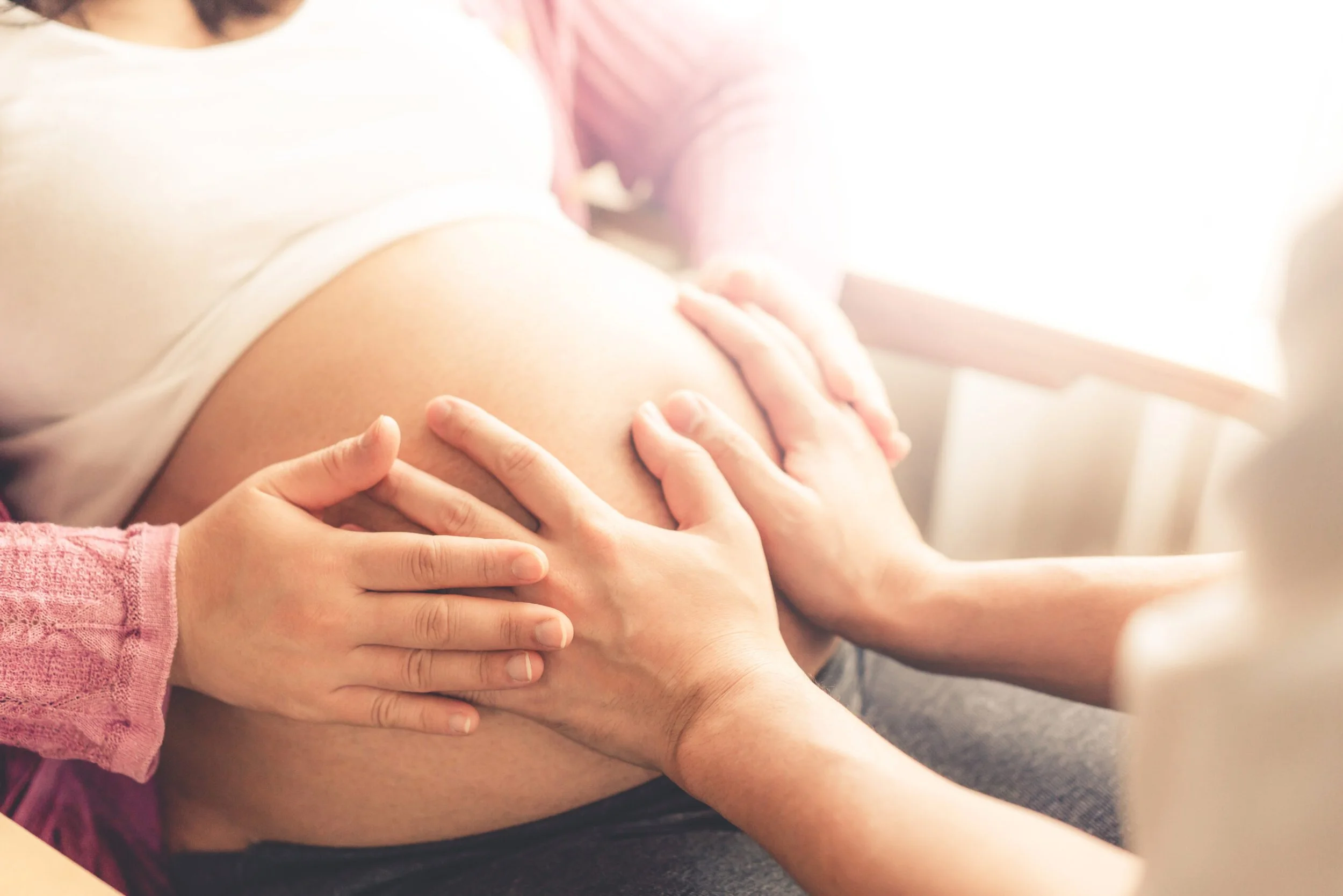Multiple hands holding a pregnant woman's belly, close-up image.