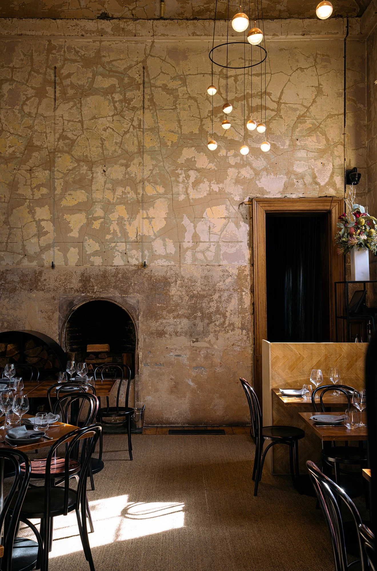 Restaurant interior with rustic exposed brick walls, modern hanging light fixtures, and set dining tables with glassware and napkins.