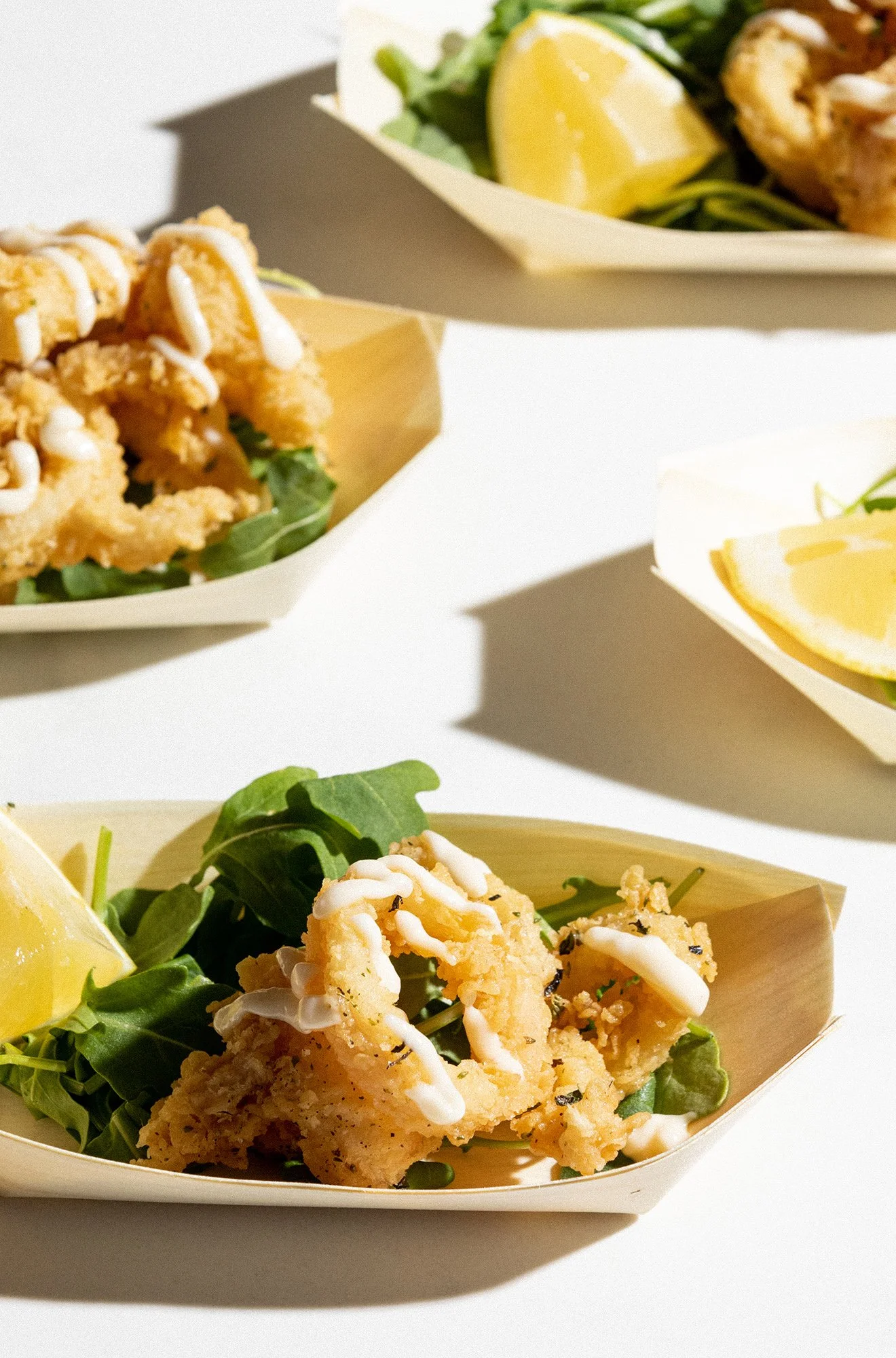 Close-up of fried calamari served on a bed of green salad with a lemon wedge, drizzled with white sauce, in a light-colored tray.