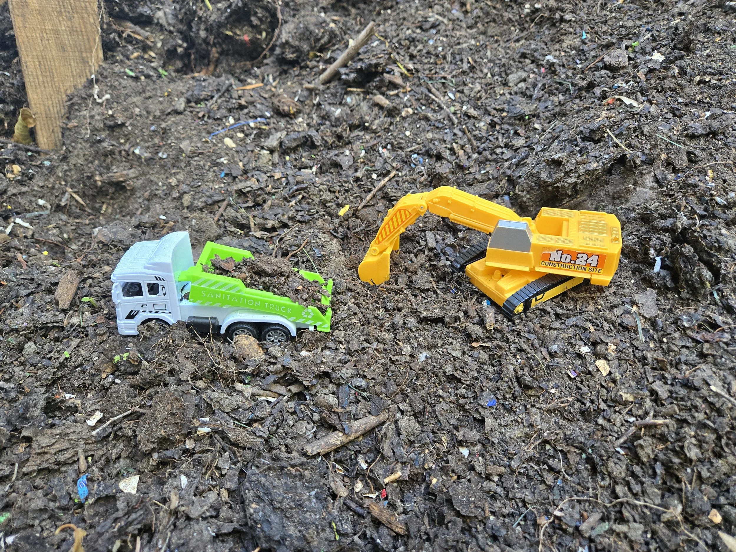 Two toy construction vehicles placed on a compost pile. Angled to represent what our composting site could look like while we work and grow towards our 1 million LBS goal.