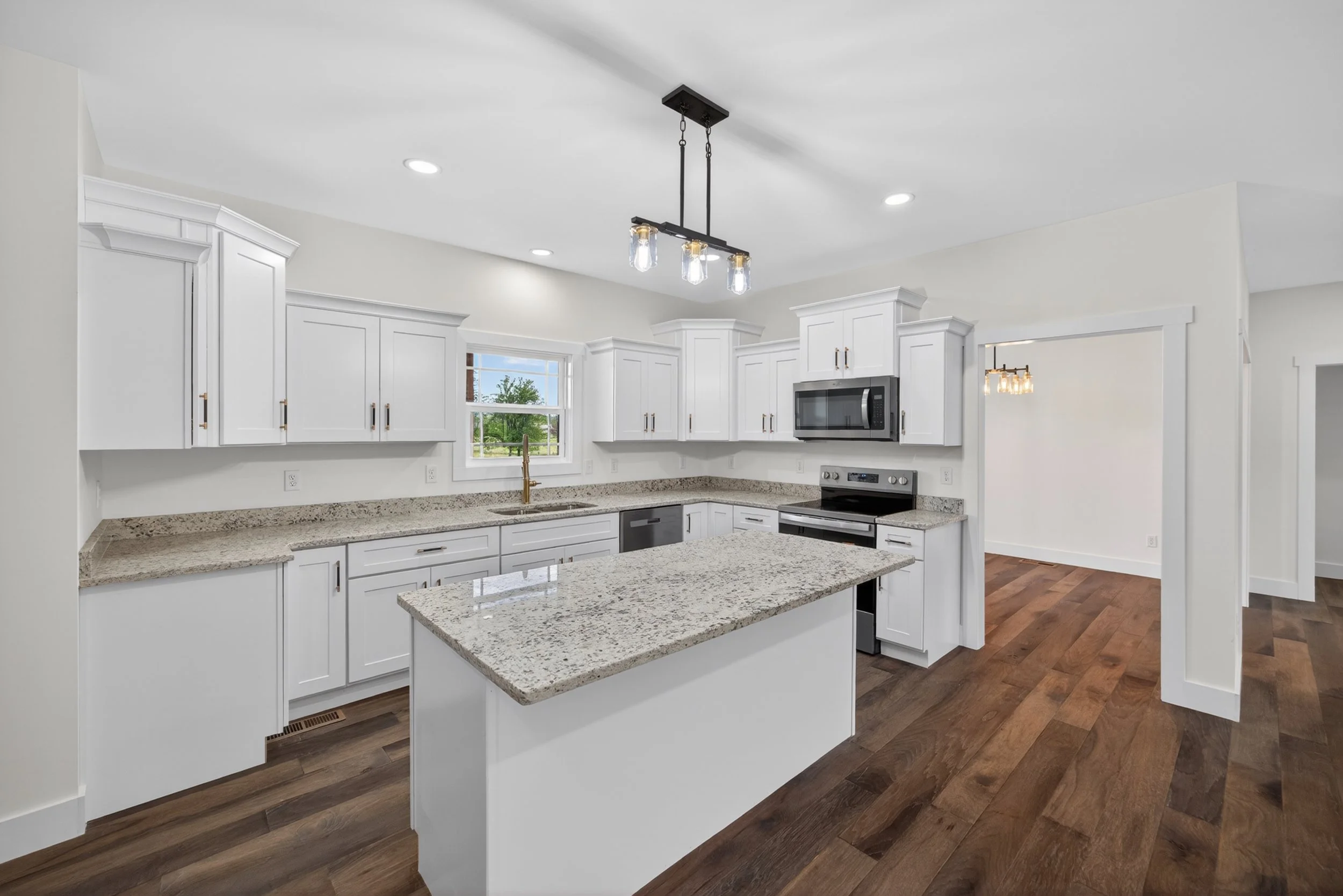 Modern white kitchen with granite countertops, stainless steel appliances, wooden floors, and pendant lighting fixtures.
