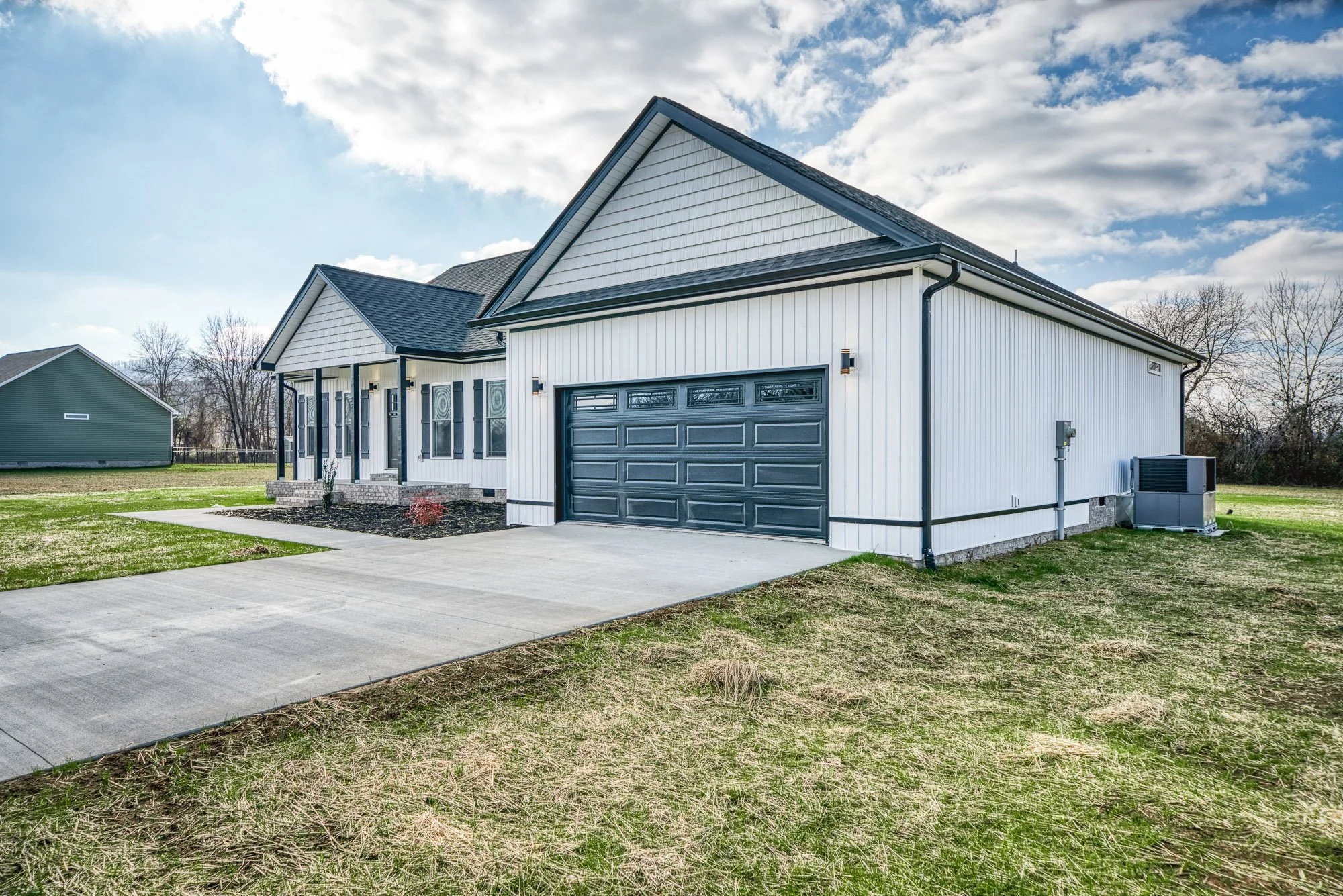 Modern house with a porch, gray garage door, and black gutters, situated on a lawn with a concrete driveway, under a partly cloudy sky.