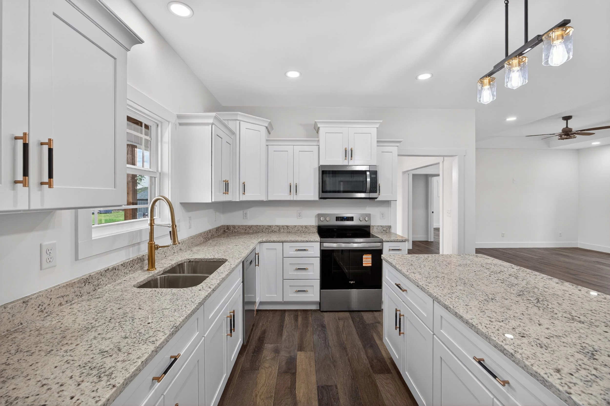 Modern kitchen with white cabinets, granite countertops, stainless steel appliances, and wooden flooring, illuminated by recessed and pendant lighting.
