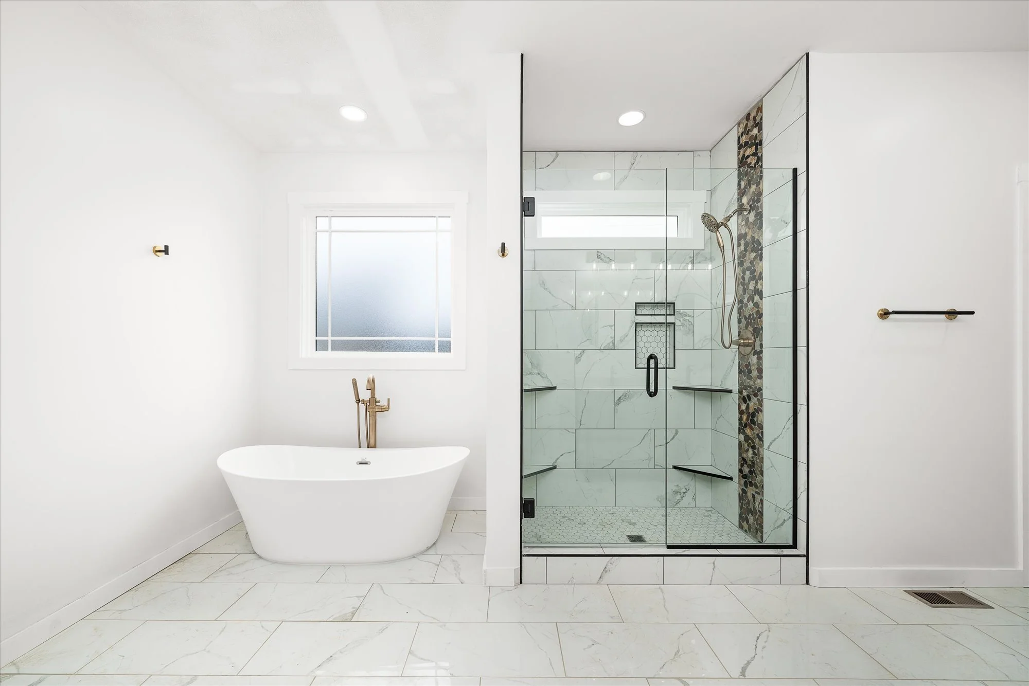 Modern bathroom with white walls, freestanding bathtub, and a glass-enclosed shower with marble tiles and pebble accent strip.