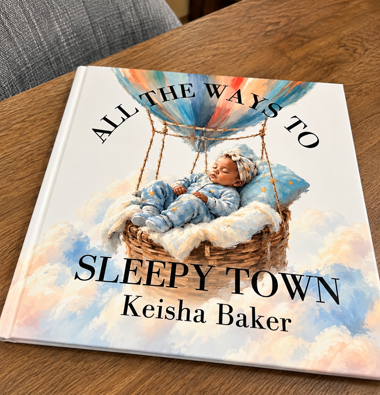 Book titled "All the Ways to Sleepy Town" by Keisha Baker featuring a painting of a sleeping baby in a basket under a hot air balloon with clouds in the background.