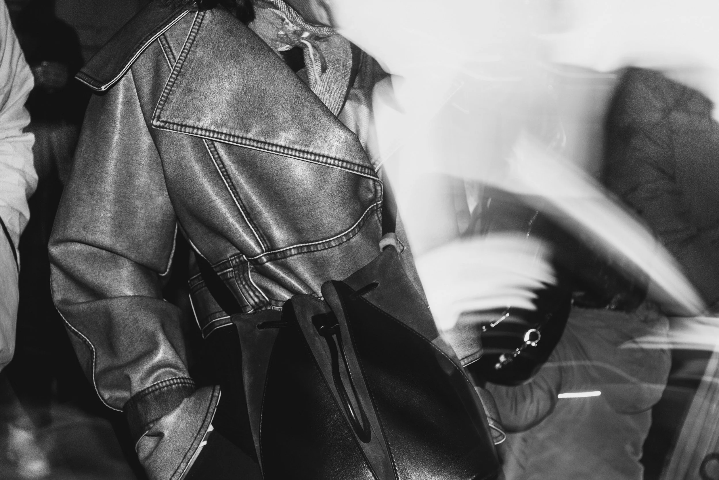 Close-up of a person wearing a leather jacket and sneakers, riding a bicycle, with motion blur indicating movement.