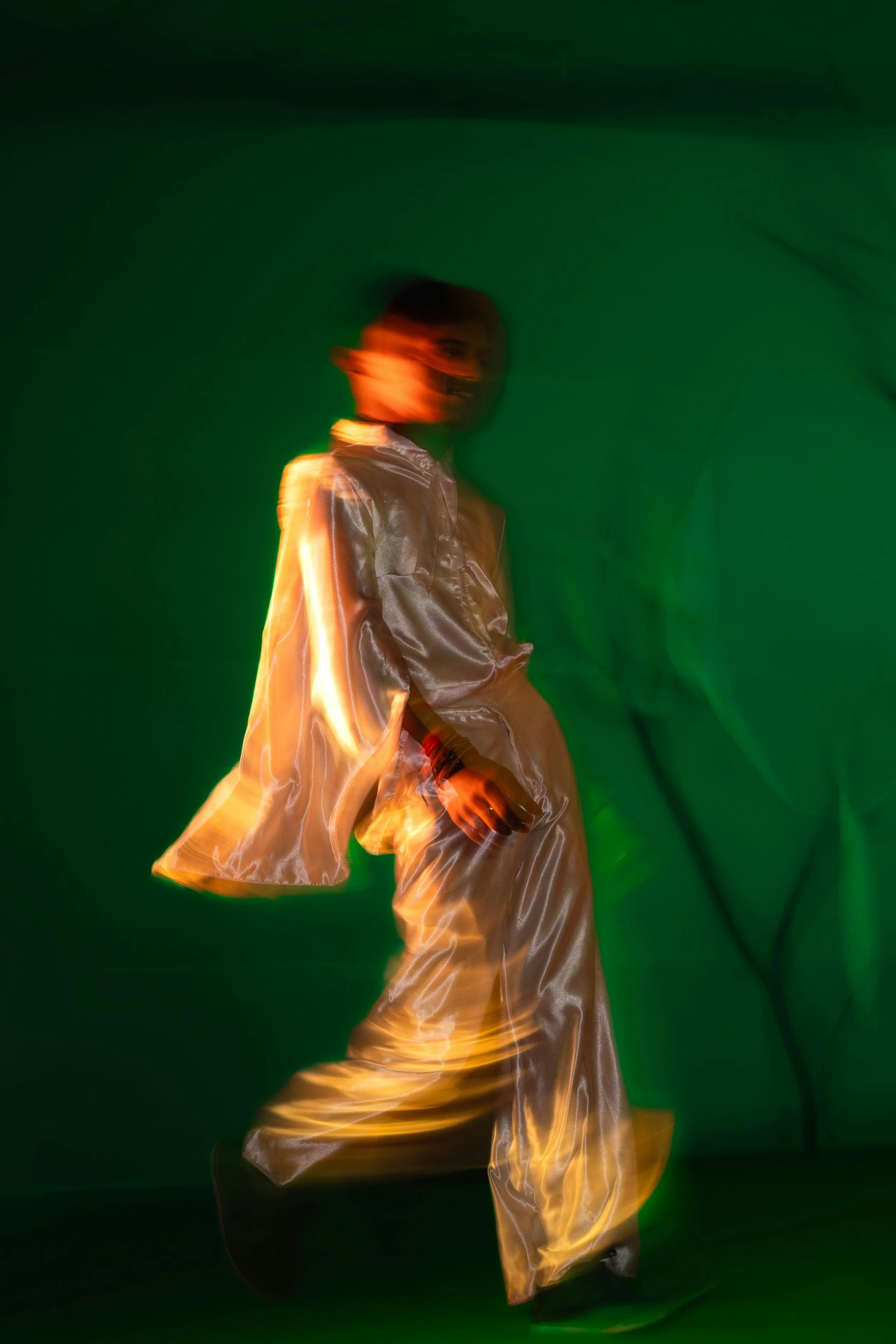 A person wearing a shiny, light-colored jacket and pants, captured with motion blur against a dark green background.