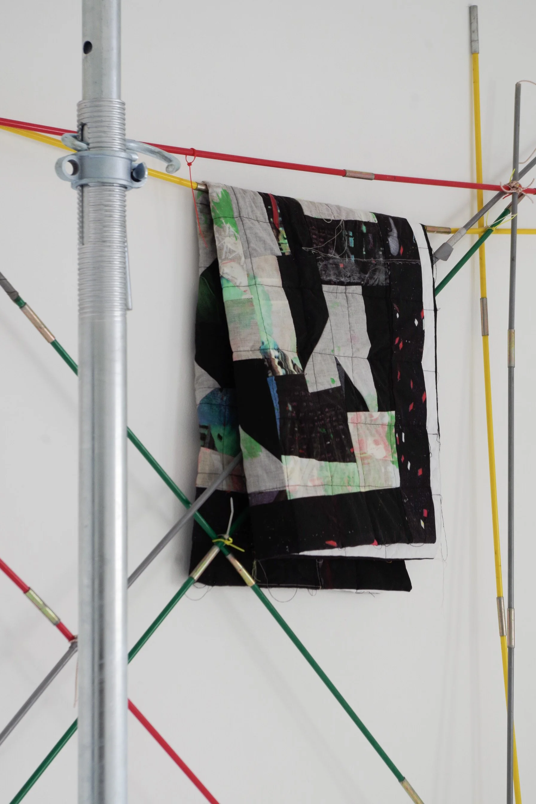 Fabric hanging on a metal frame with colorful rods arranged in a geometric pattern against a plain white wall.