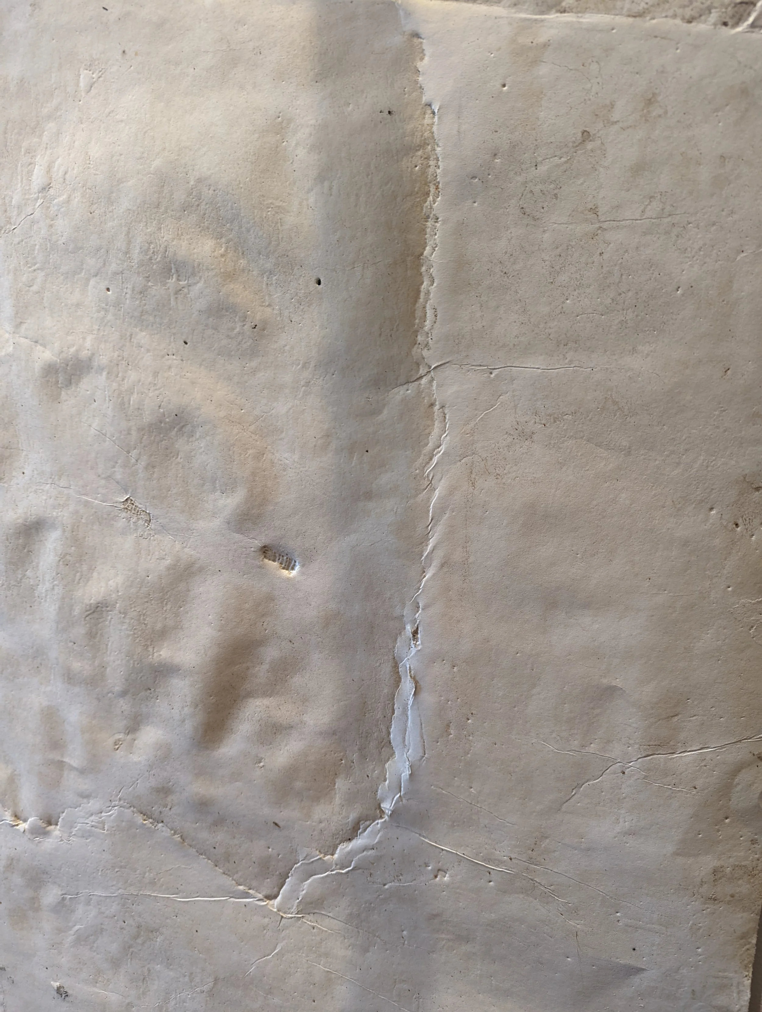 Close-up of an old, cracked, beige-colored wall or surface with peeling paint and small imperfections.