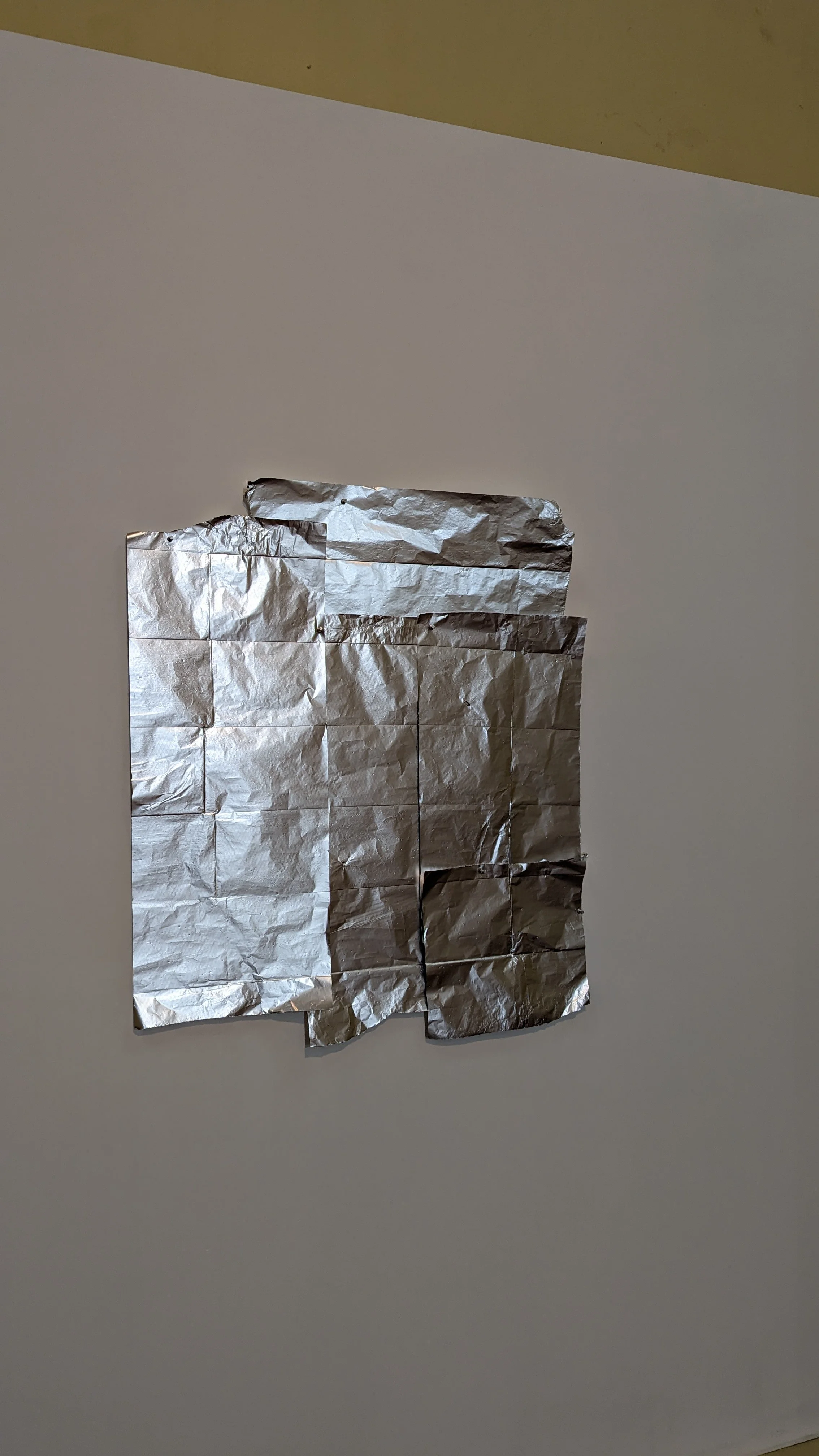 A small sheet of crinkled aluminum foil stuck to a white wall.