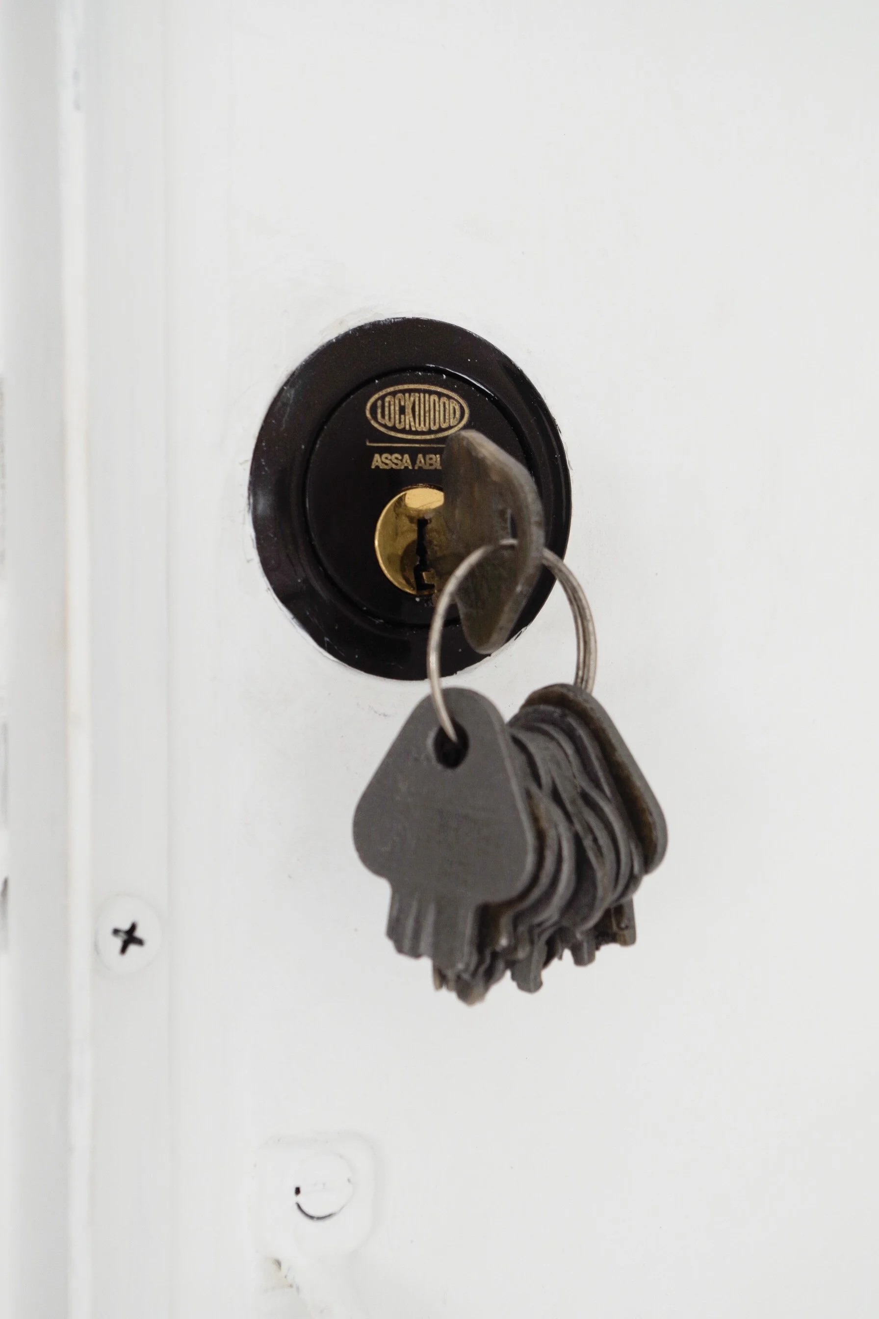 A set of keys hanging on a black Lockwood lock with a smiley face on a white wall.