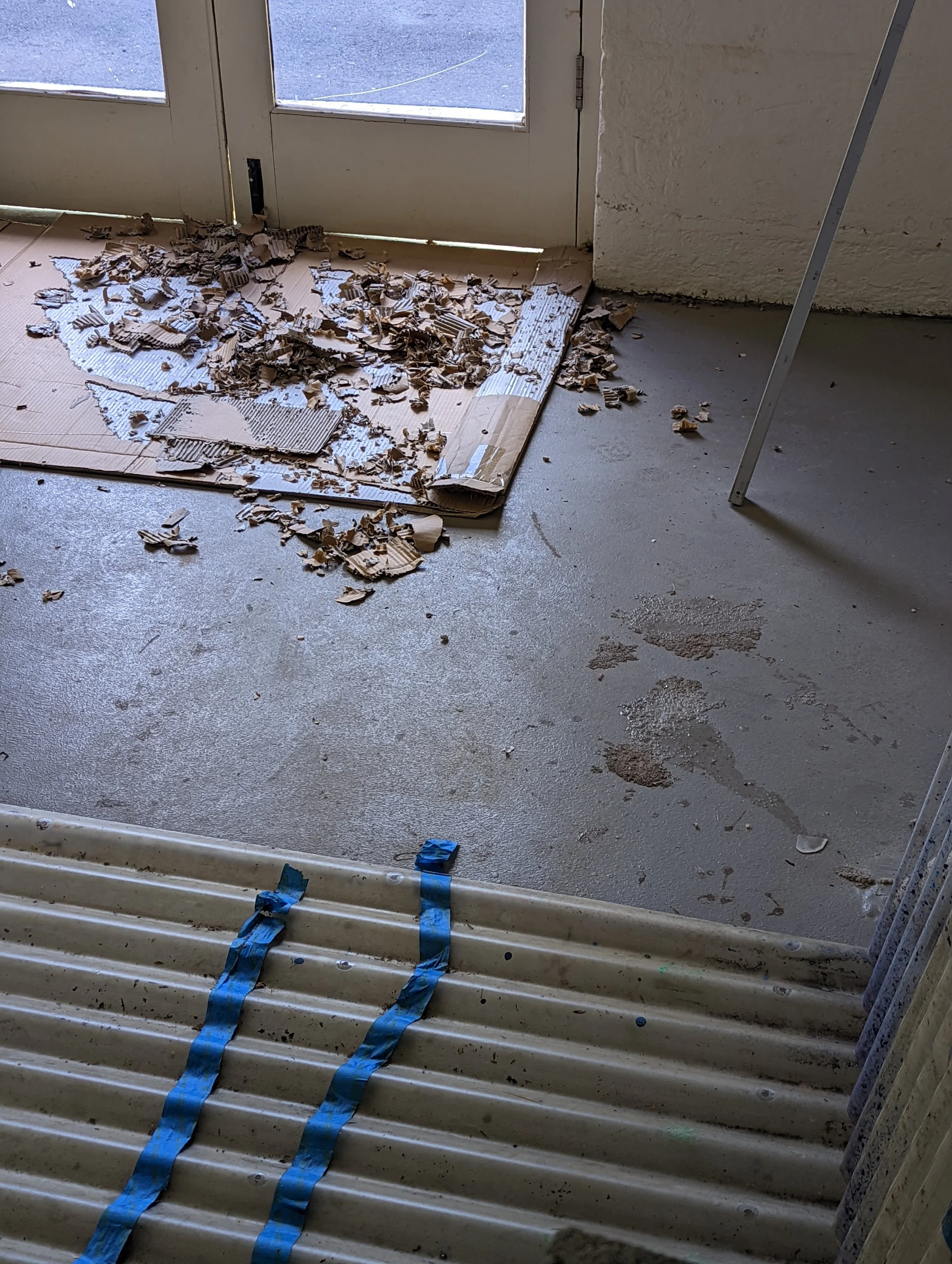 Broken cardboard and packing paper on a tiled floor near glass door, with tools and construction debris nearby, suggesting a renovation or moving activity.