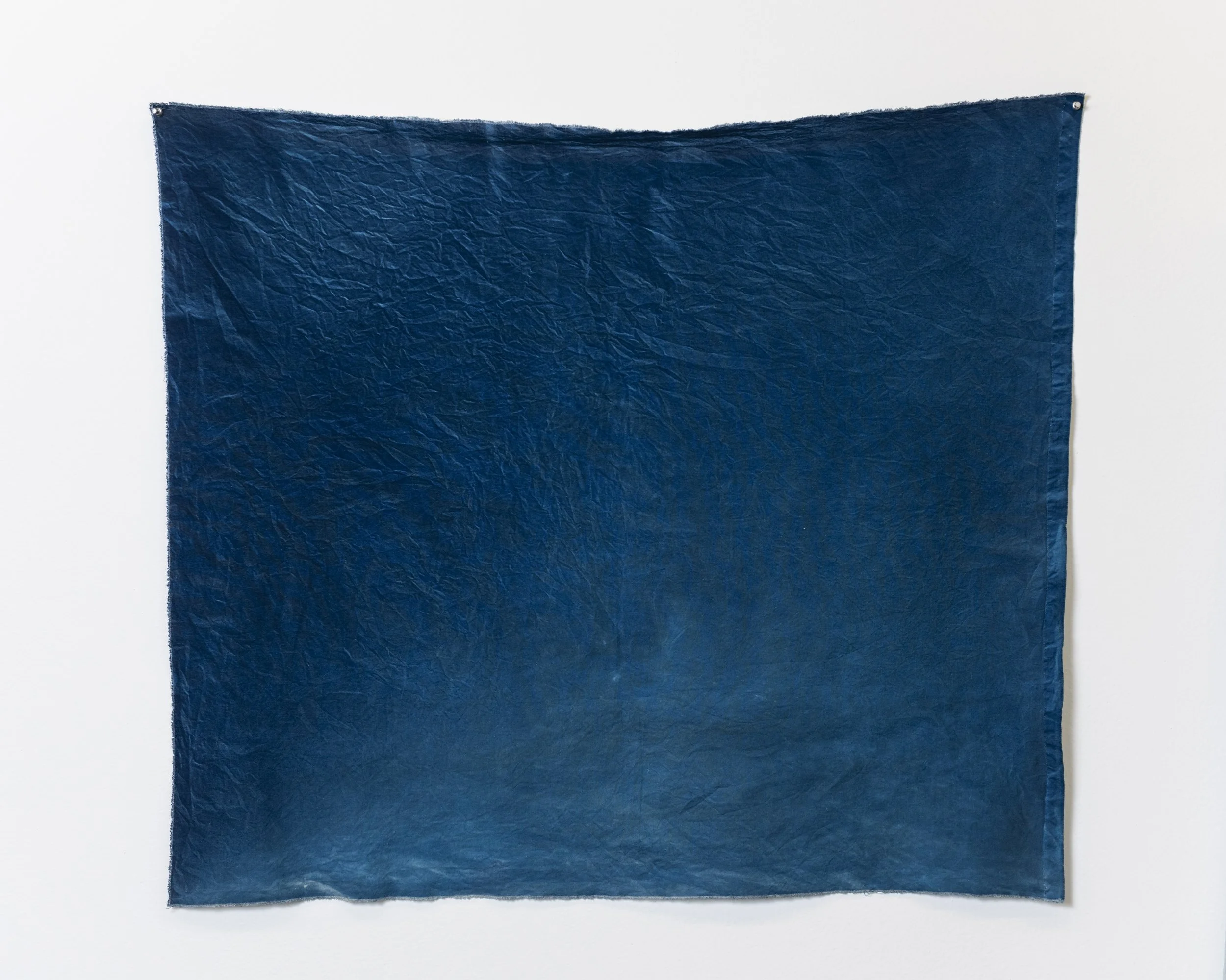 A blue textured fabric hanging on a wall with metal fasteners in the top corners.